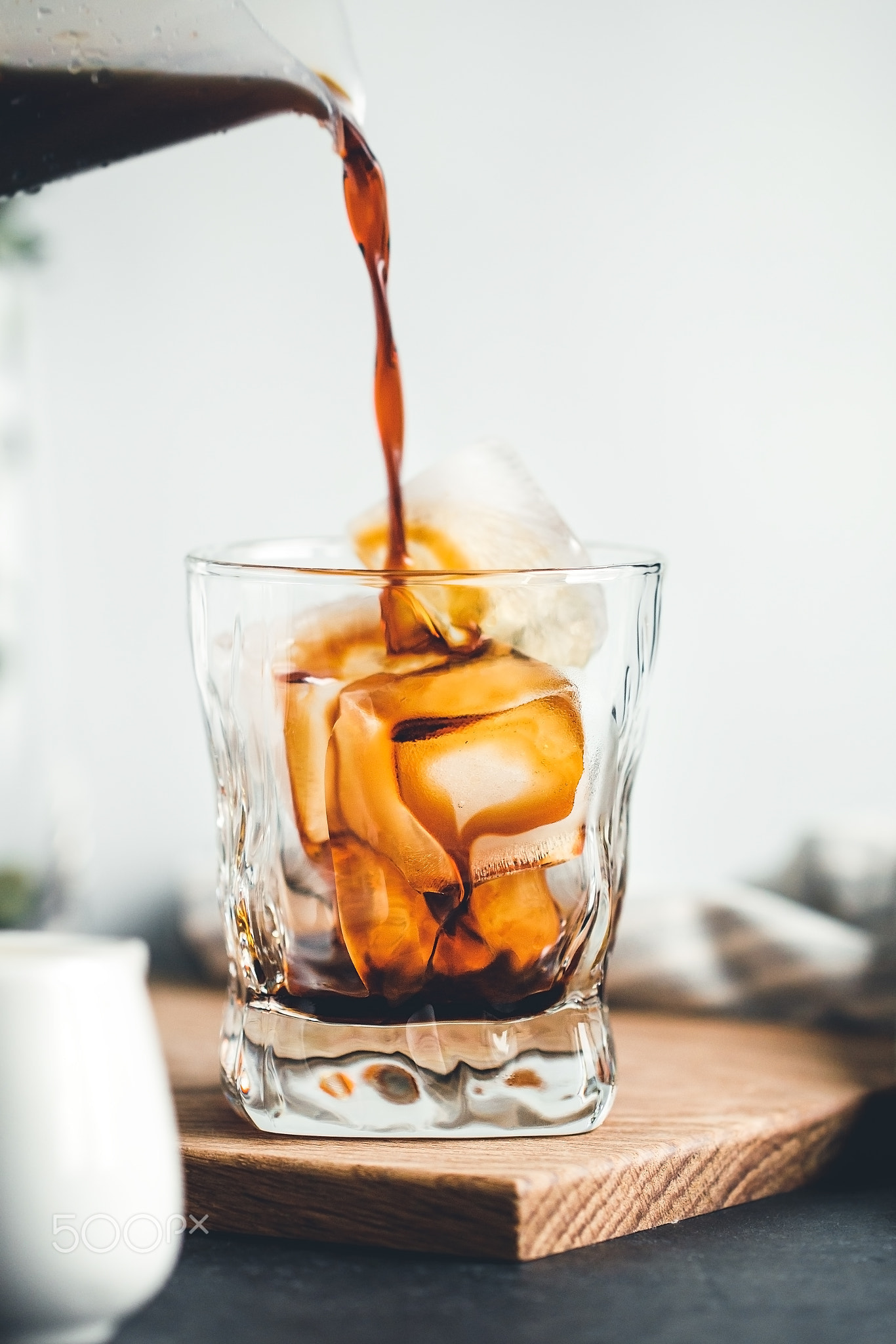 Pouring cold espresso in a glass with ice cubes in a modern kitchen in the morning.