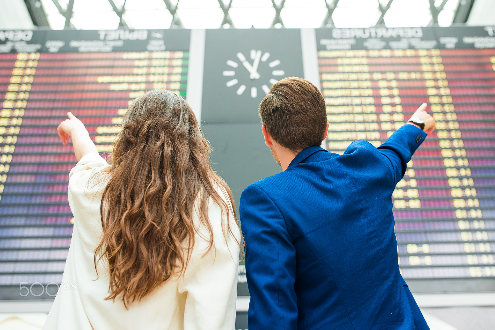 Young man and woman in international airport looking at the flight information board