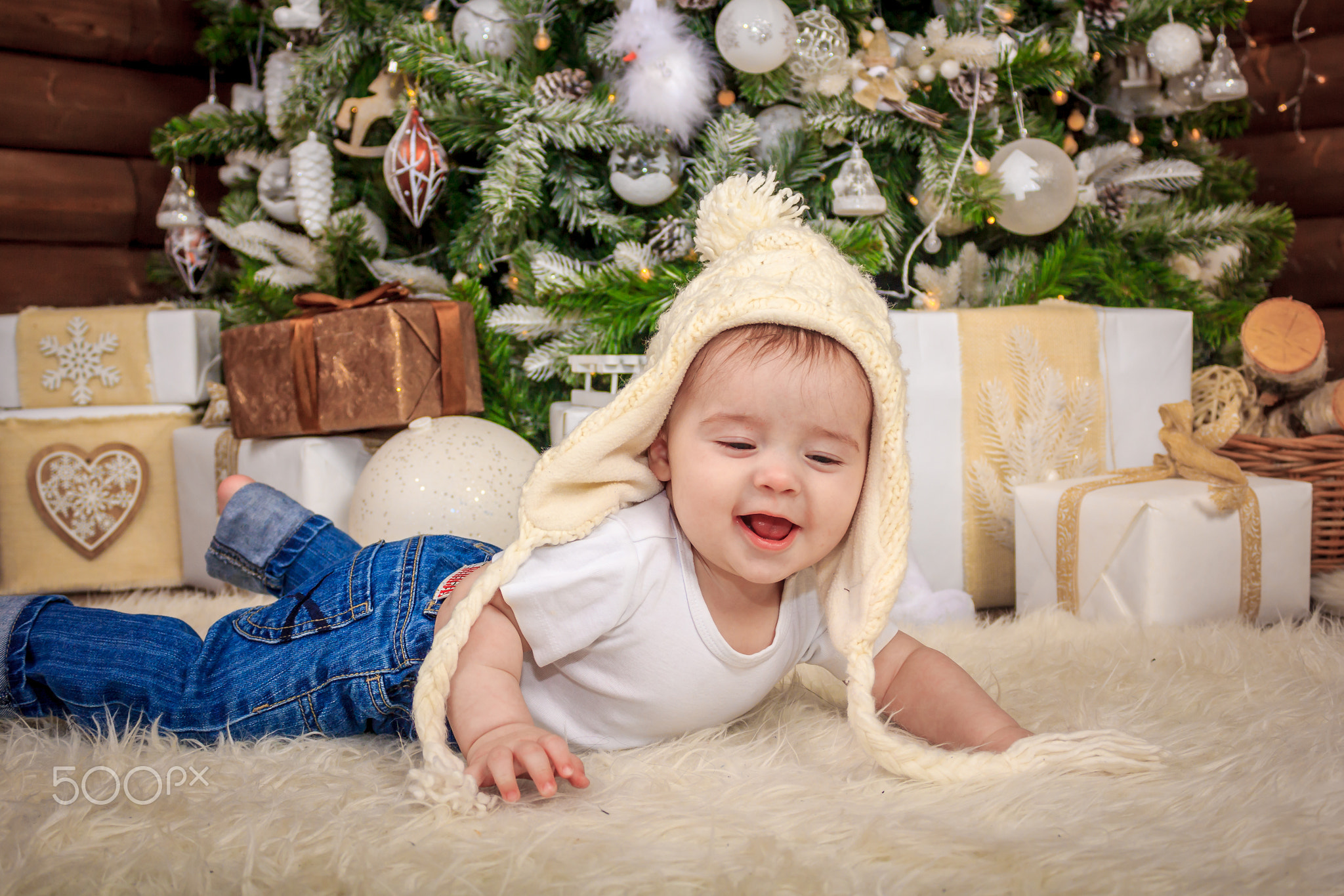 Baby in elf costume playing with old wooden train and soft toy bears under the Christmas tree,...