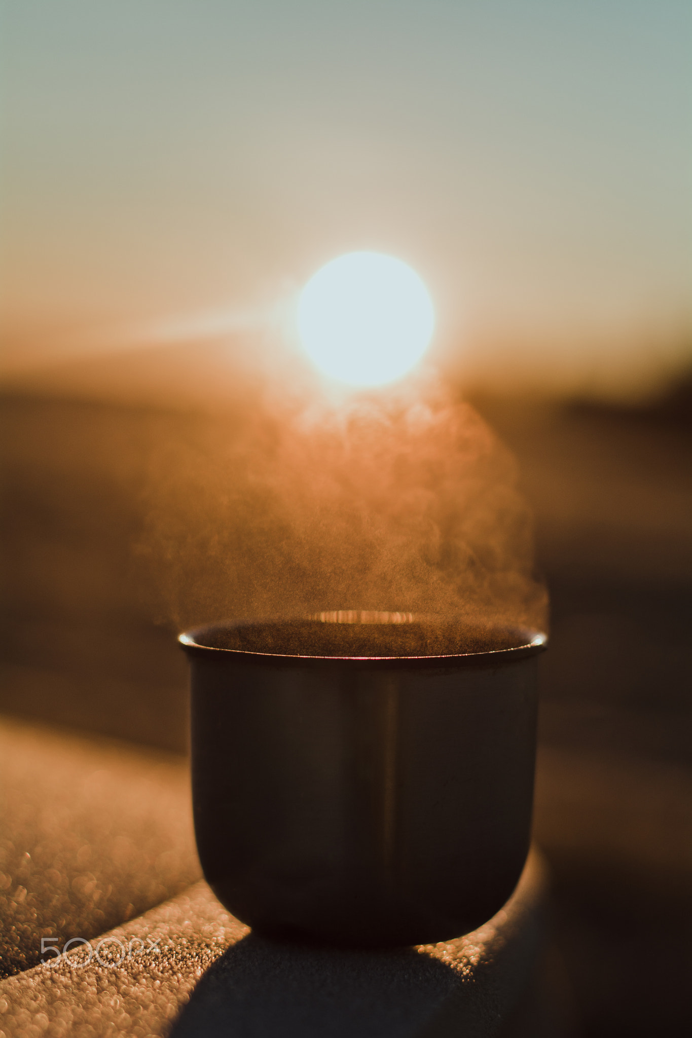 Steam from a hot tea mug from a thermos, which is illuminated by the winter morning sun in the...