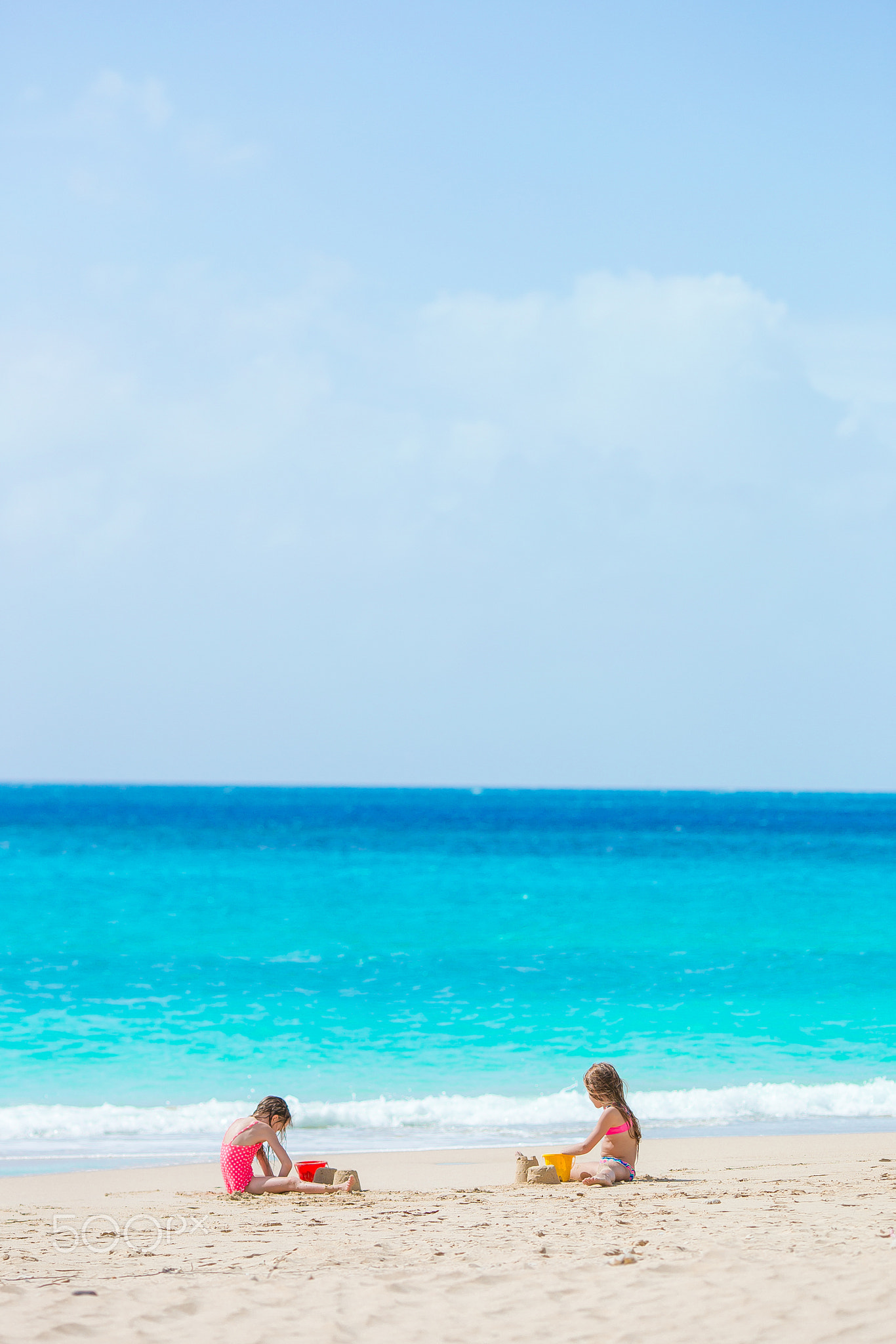Two kids making sand castle and having fun at tropical beach