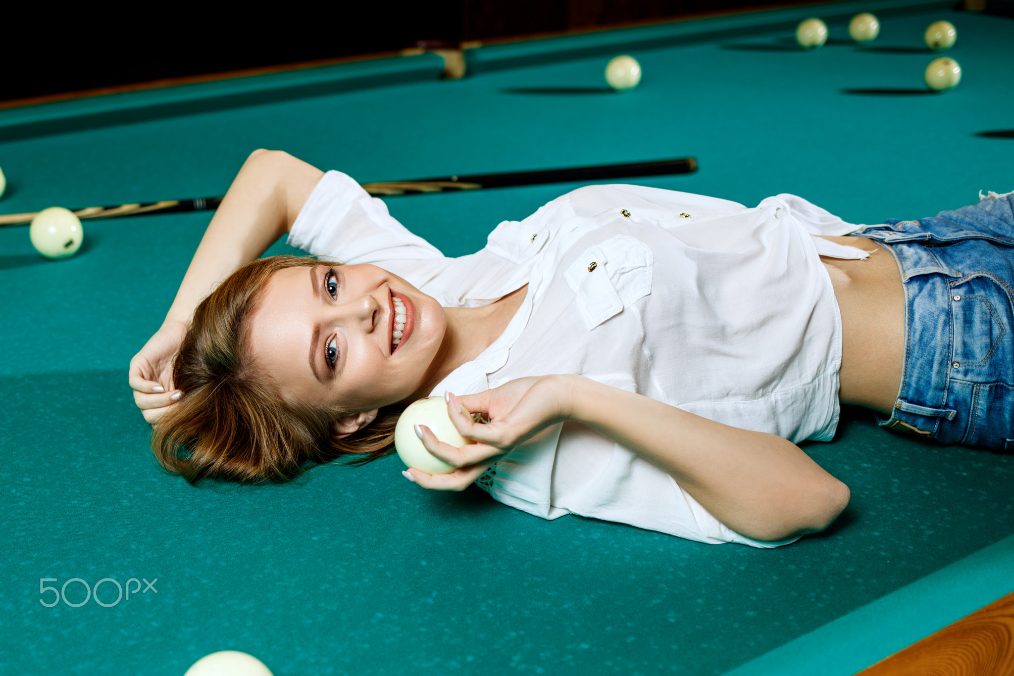 Young woman lying on the billiard table and looking at camera.