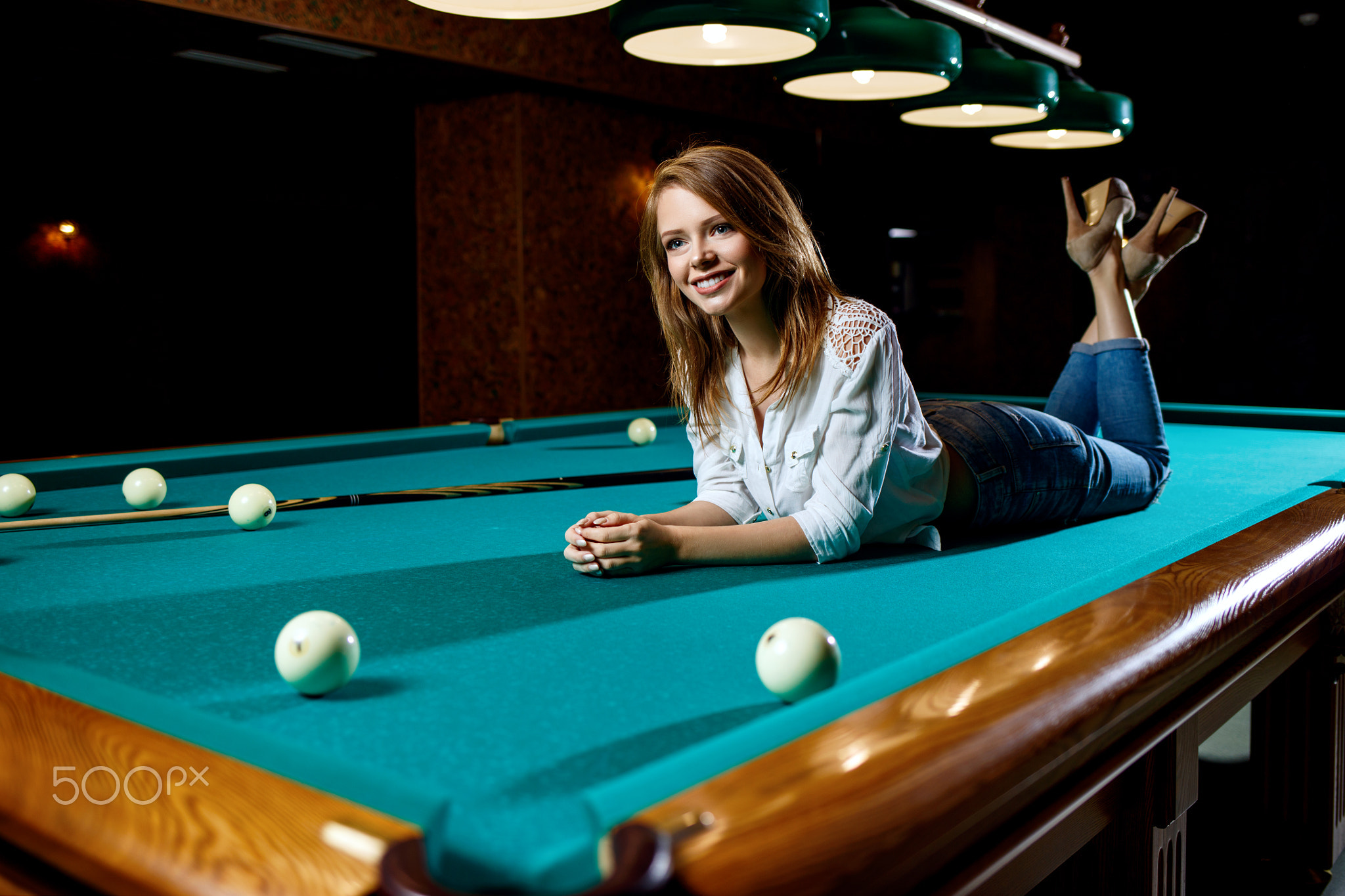 Young woman lying on the green billiard table.