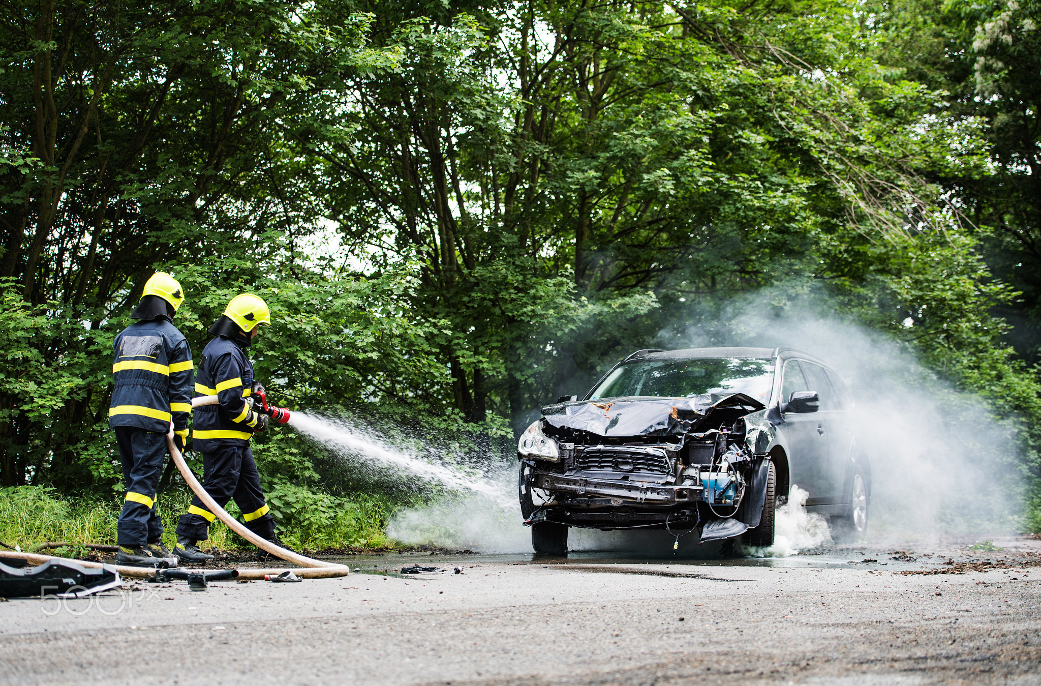 Two firefighters extinguishing a burning car after an accident.