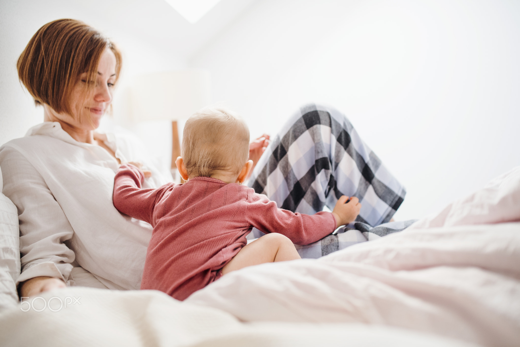 A young mother with little daughter sitting indoors on bed in the morning, playing.