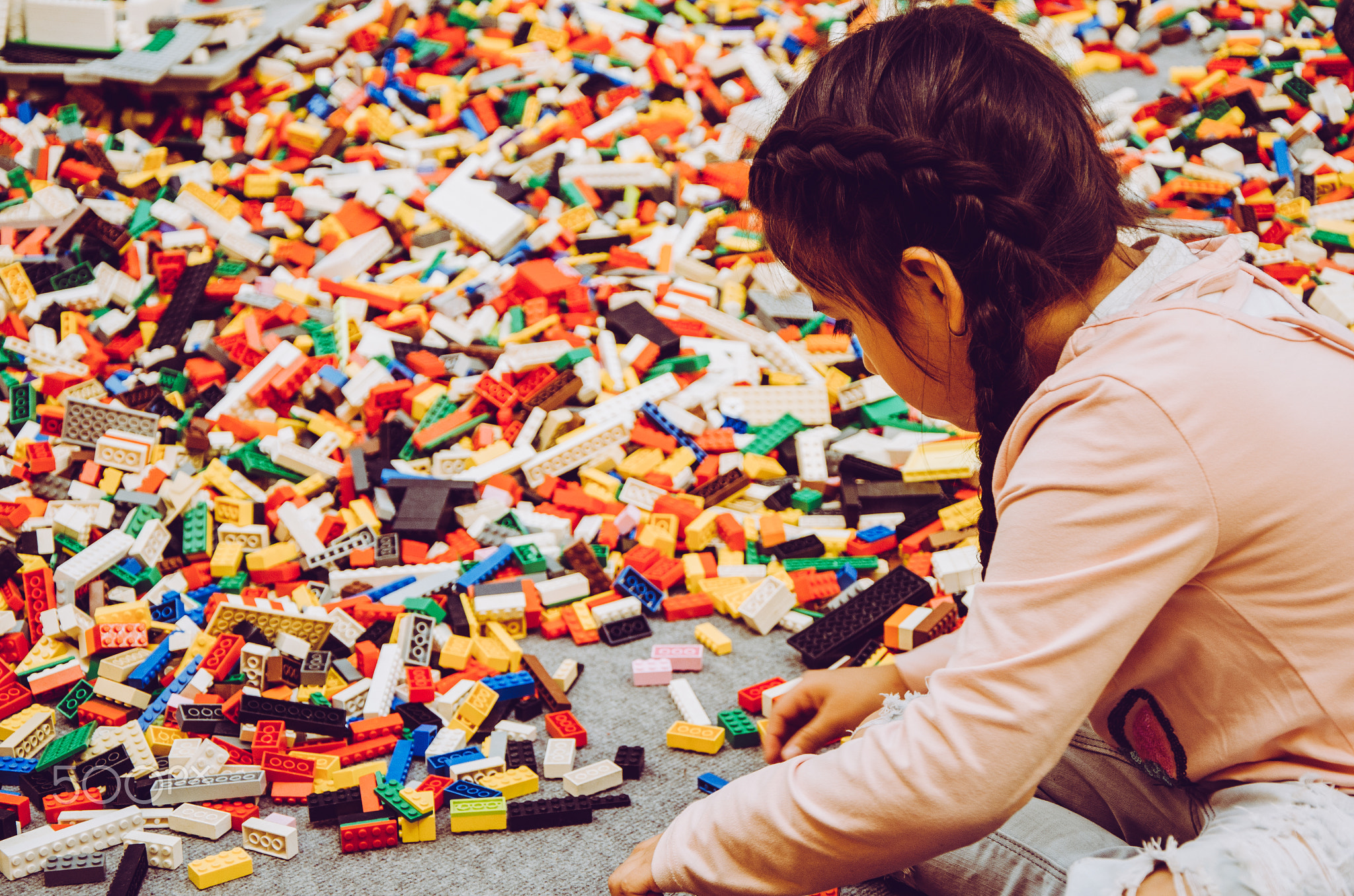 Little girl playing with many plastic building bricks parts