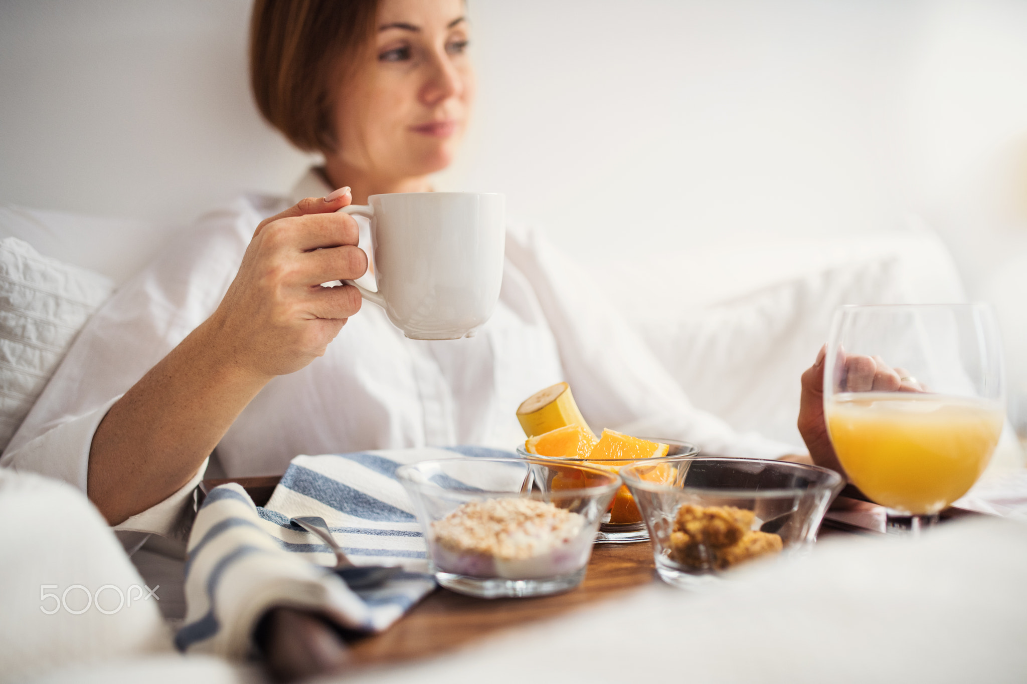 A woman with breakfast in bed in the morning, using smartphone.