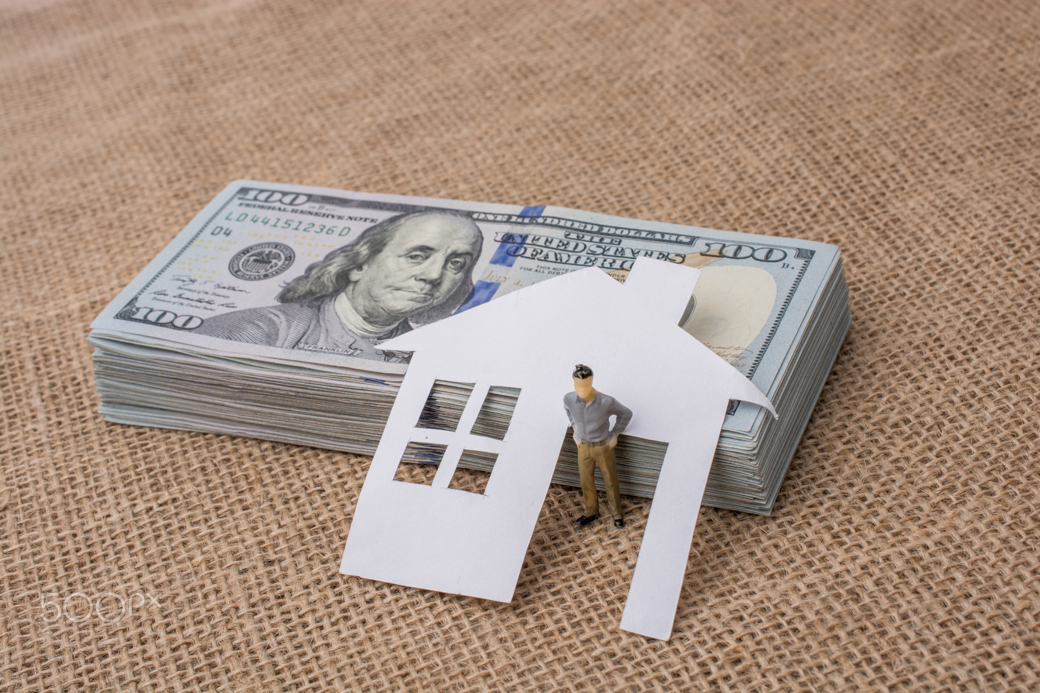 Paper house and a man figurine beside US dollar banknote