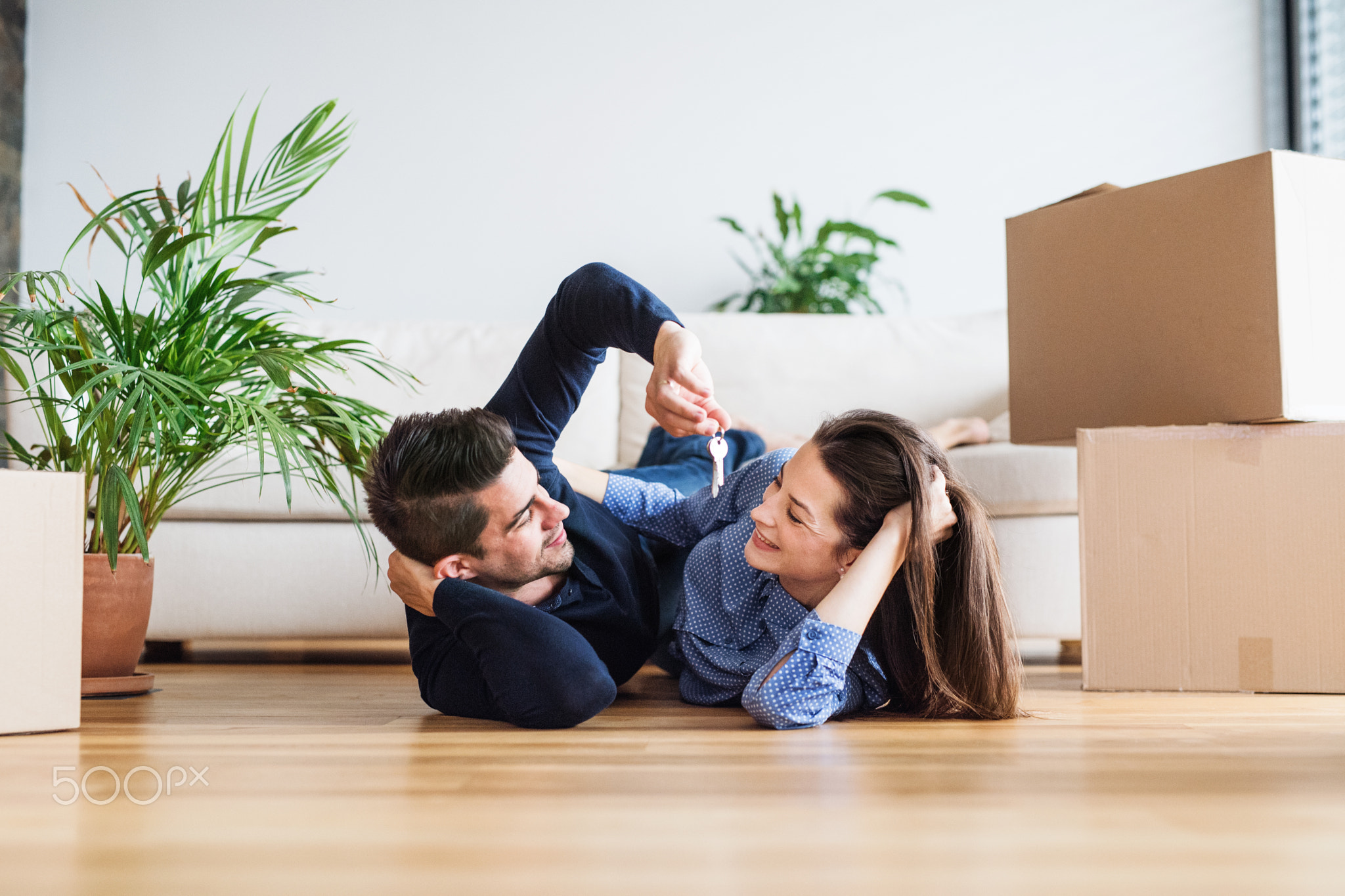 A young couple with a key and cardboard boxes moving in a new home.