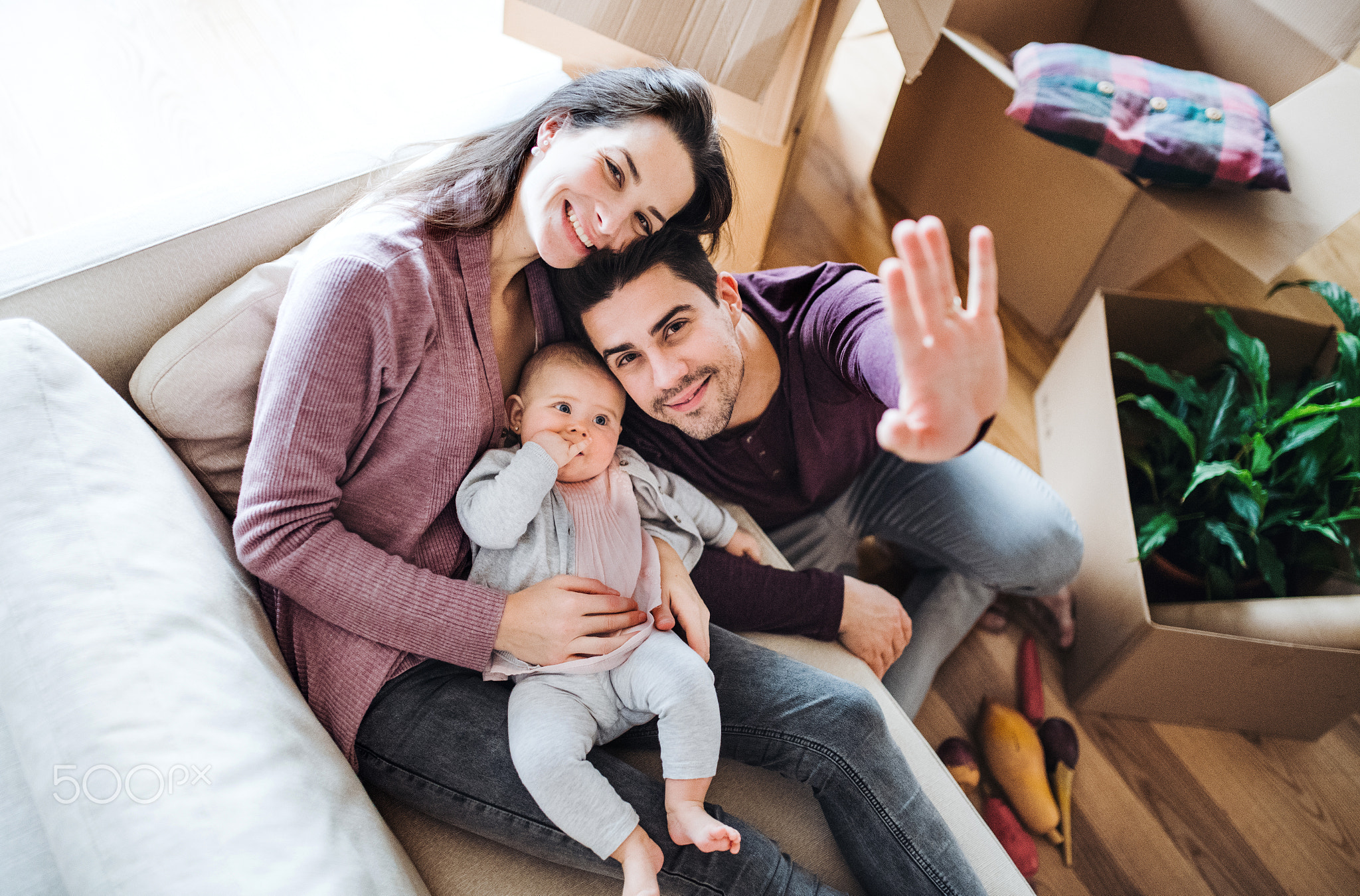 A portrait of young couple with a baby and cardboard boxes moving in a new home.