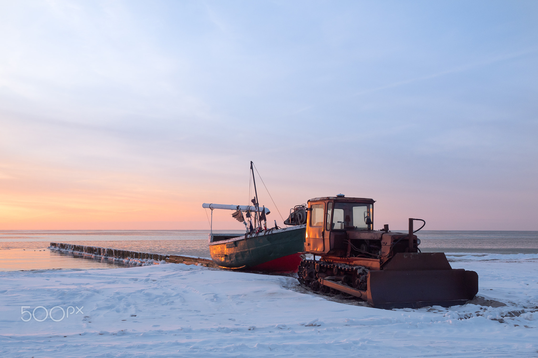 Tractor pulls a fishing boat on the shore.