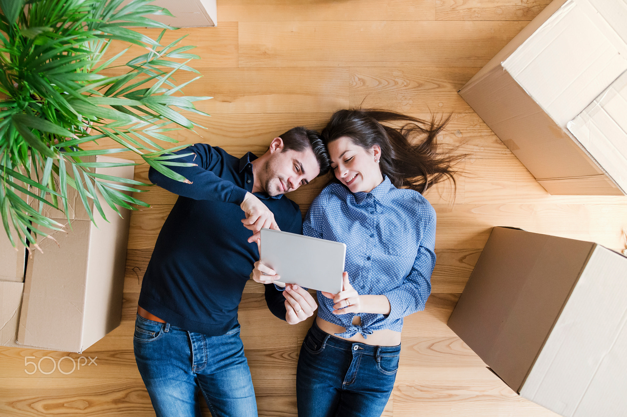 A top view of young couple with tablet and cardboard boxes moving in a new home.