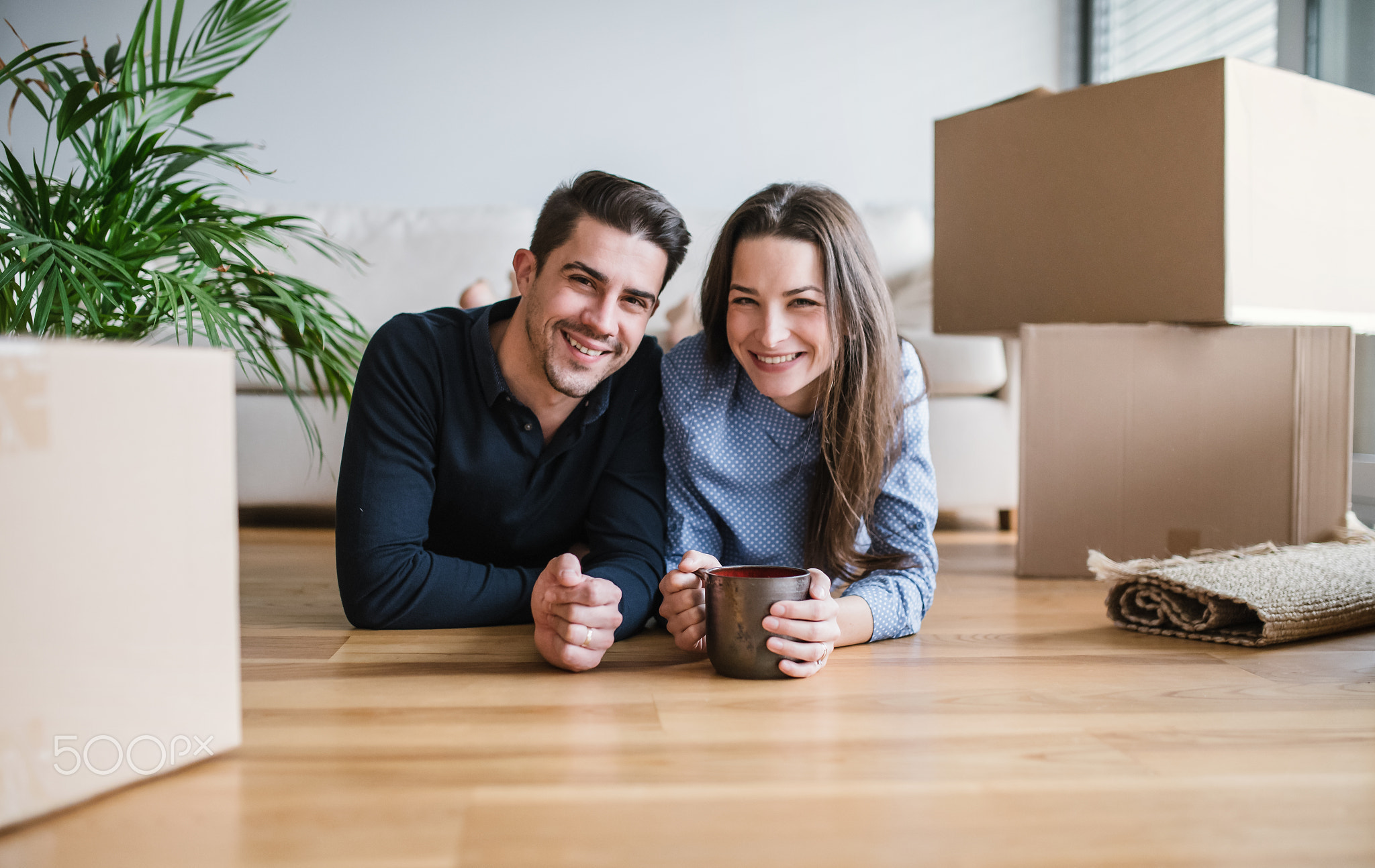 A young couple with a cup and cardboard boxes moving in a new home.