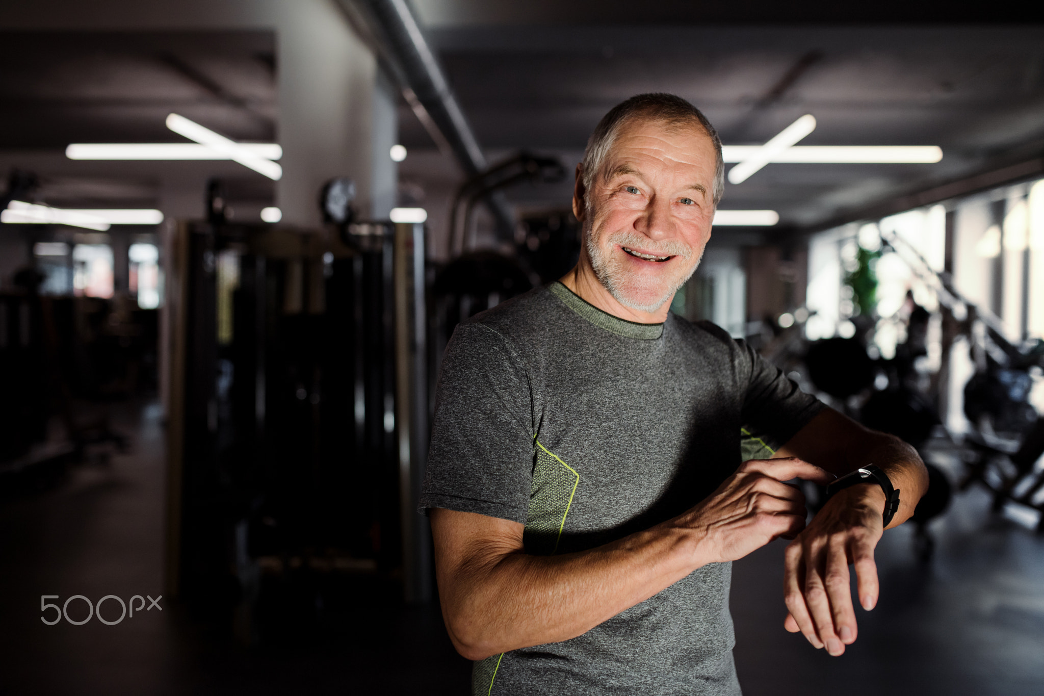 A cheerful senior man in gym measuring time while doing exercise. Copy space.