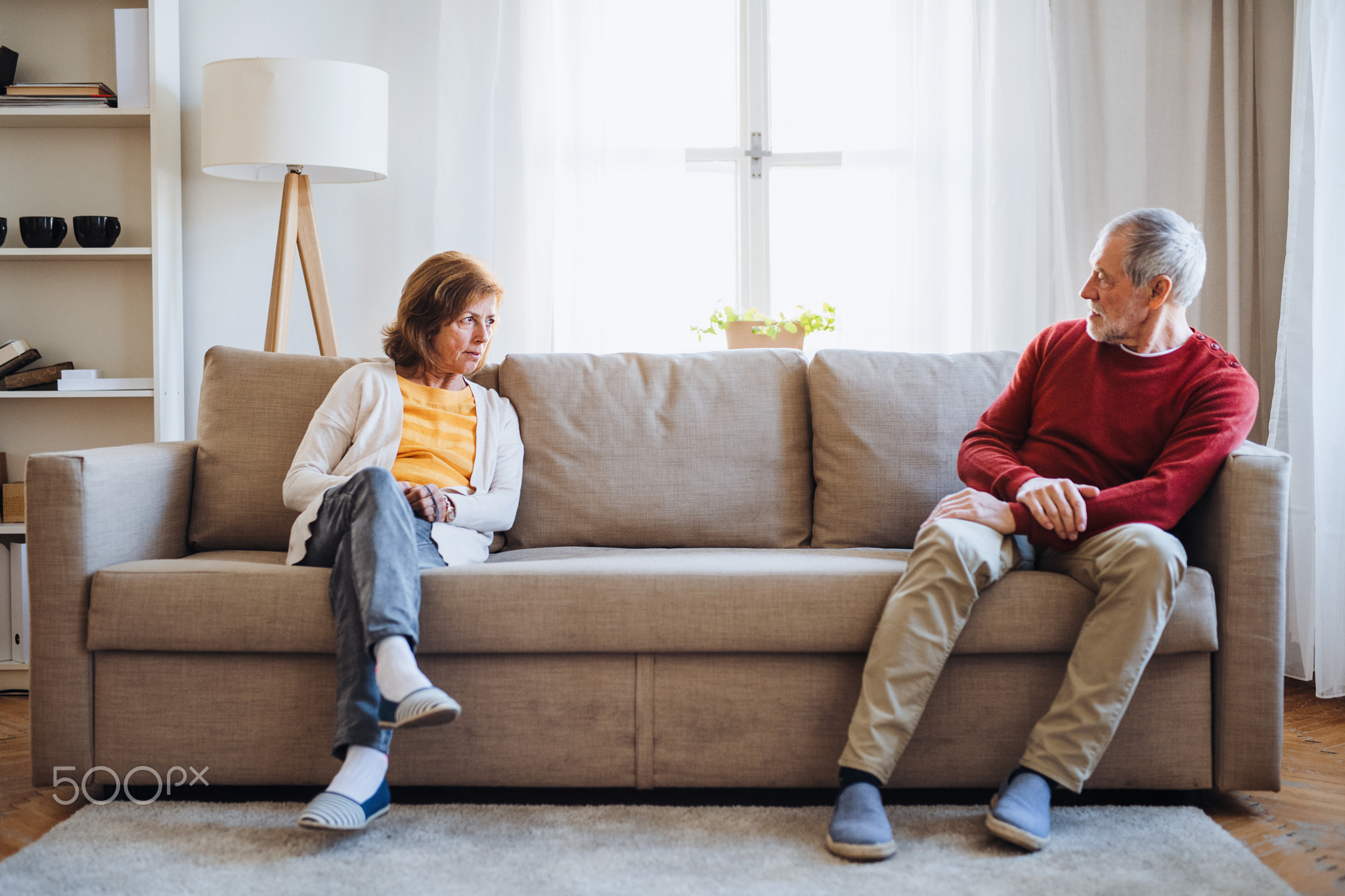 A senior couple sitting on a sofa at home, having an argument.