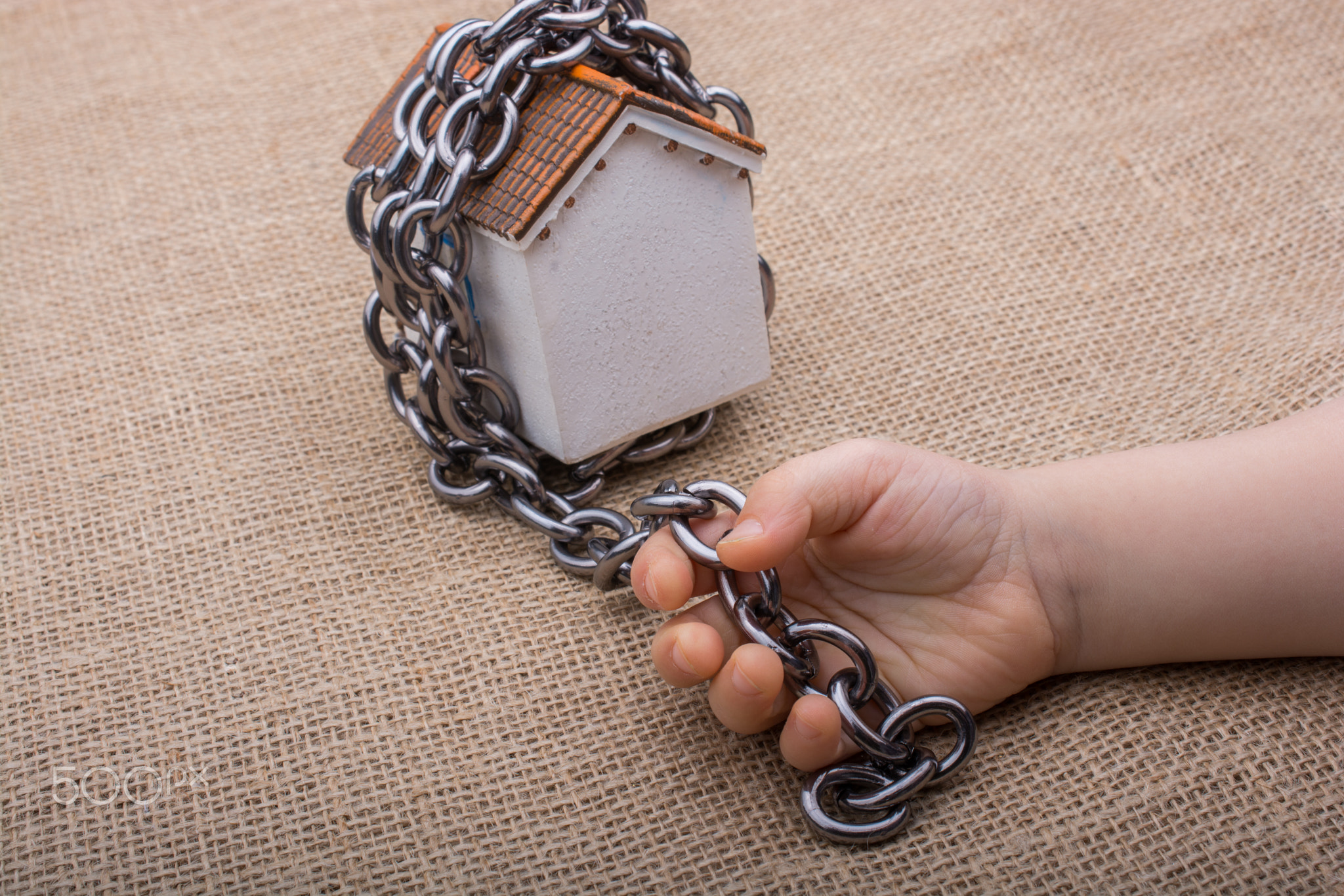 Little hand holding a chain around a model house