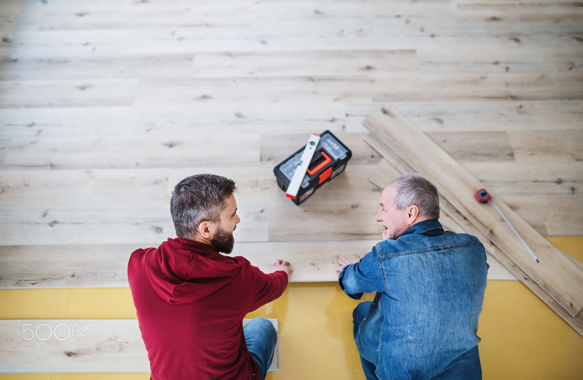 A mature man with his senior father laying wood flooring, a new home concept.