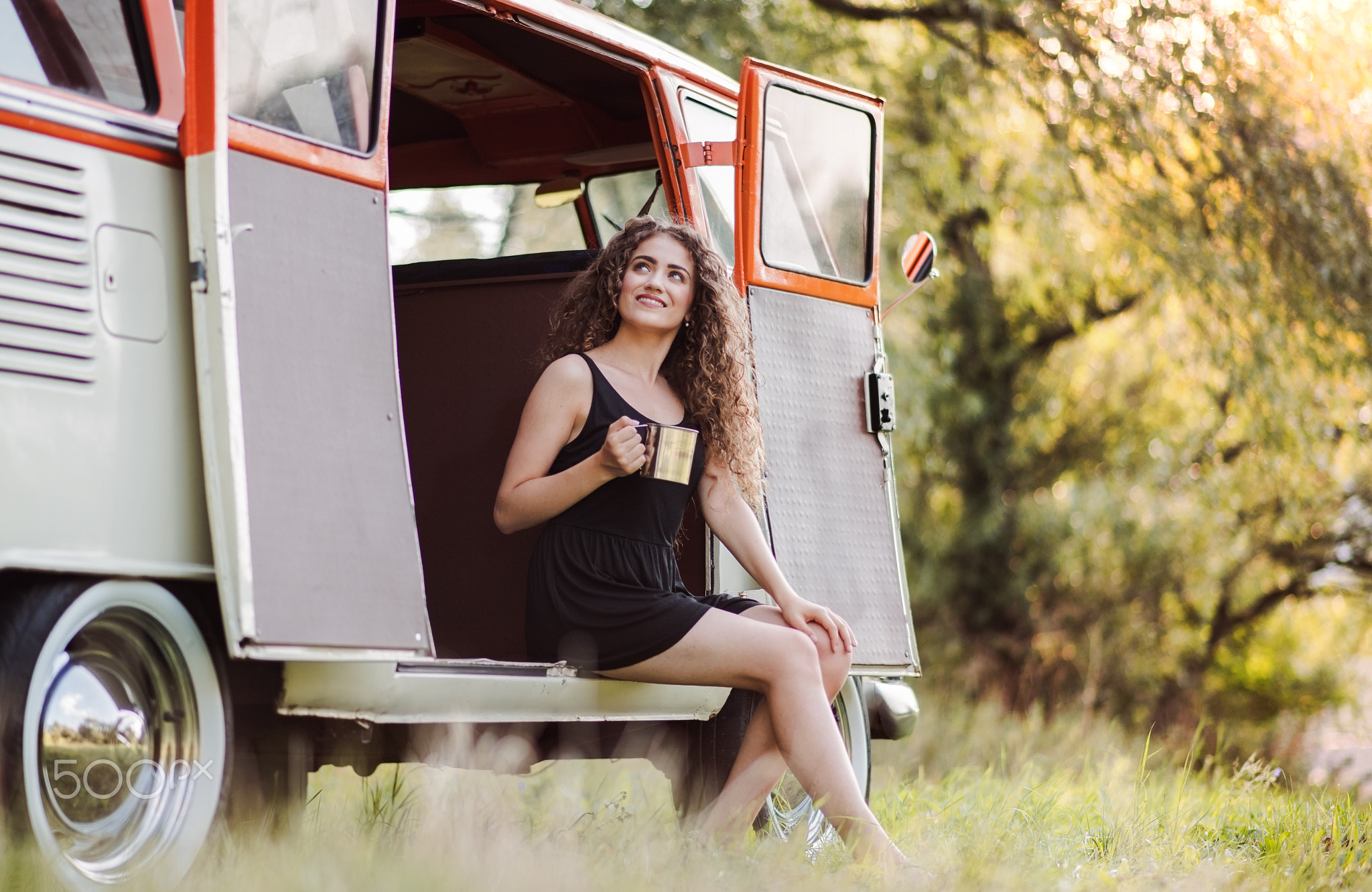 A young girl sitting in the boot of a car on a roadtrip through countryside.