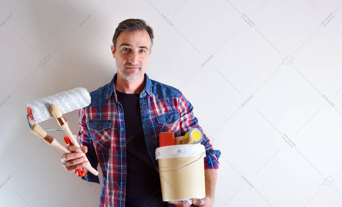 Man with paint tools on hands and white wall behind