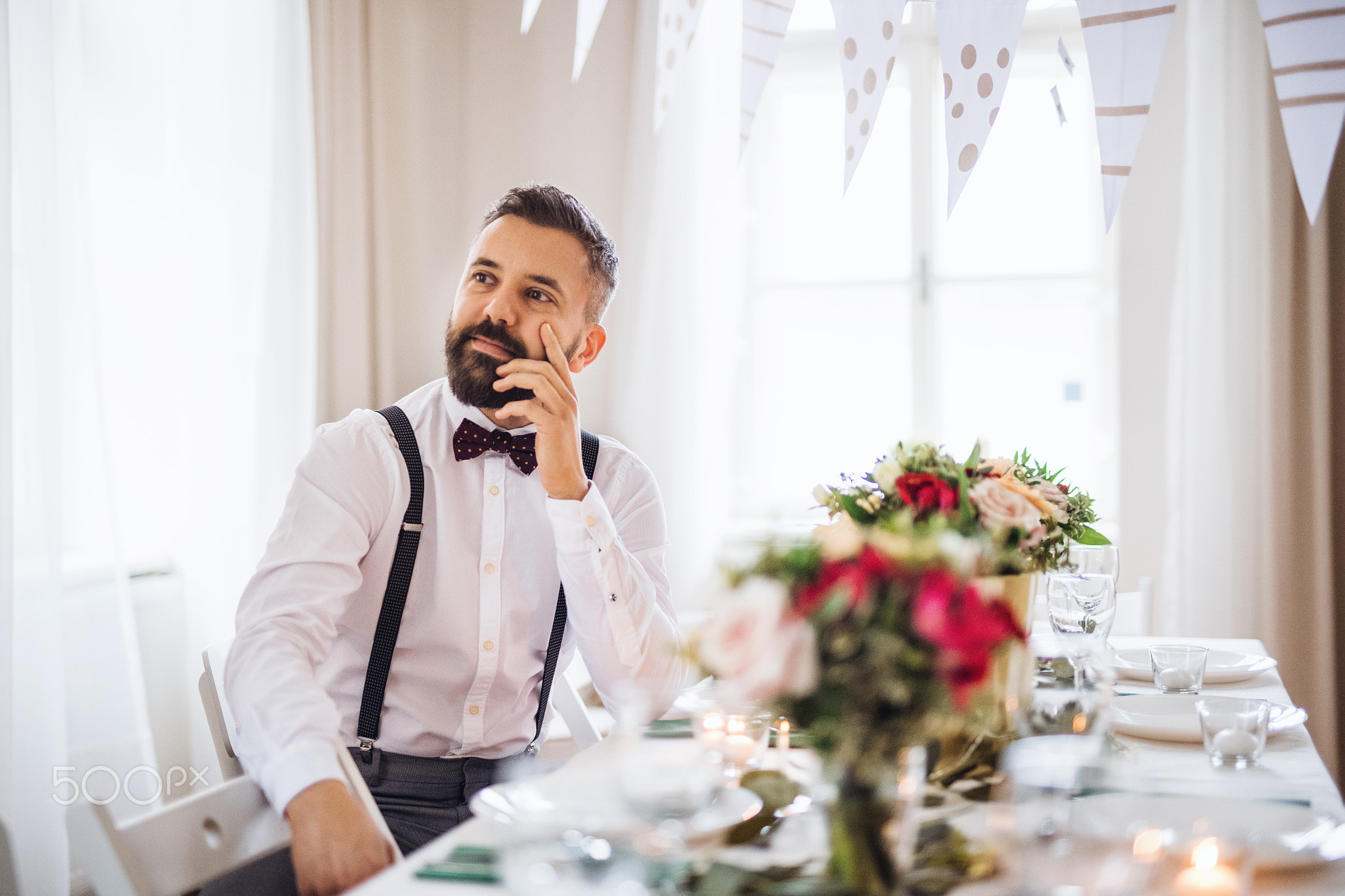 A portrait of a thoughtful mature man sitting indoors in a room set for a party.