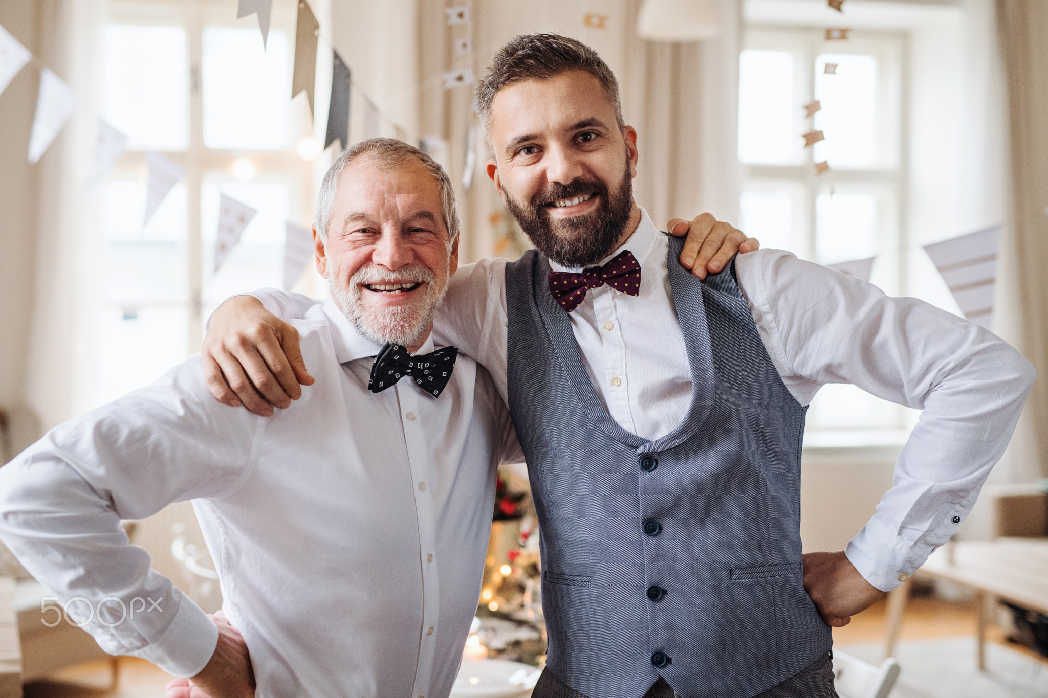 A portrait of a senior and mature man standing indoors in a room set for a party.