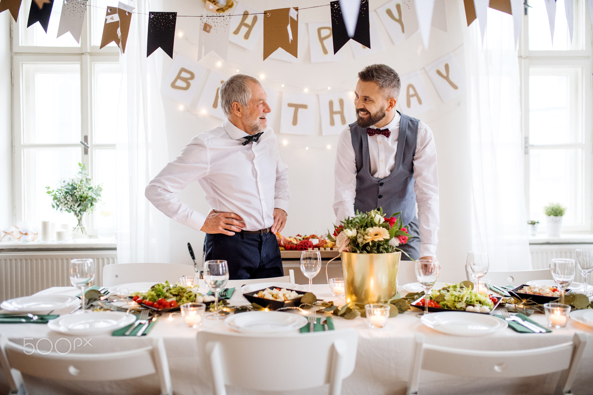 A portrait of a senior and mature man standing indoors in a room set for a party.