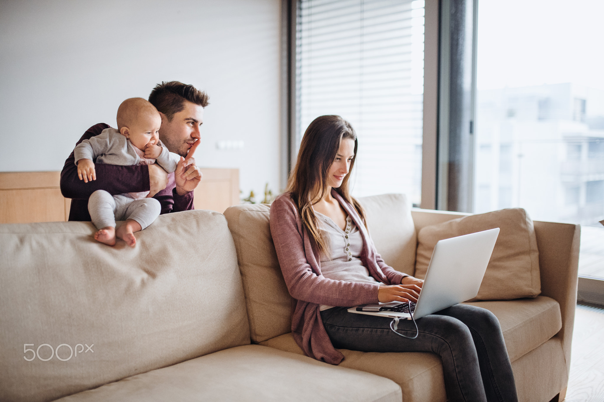 A portrait of young couple with a baby and laptop at home.