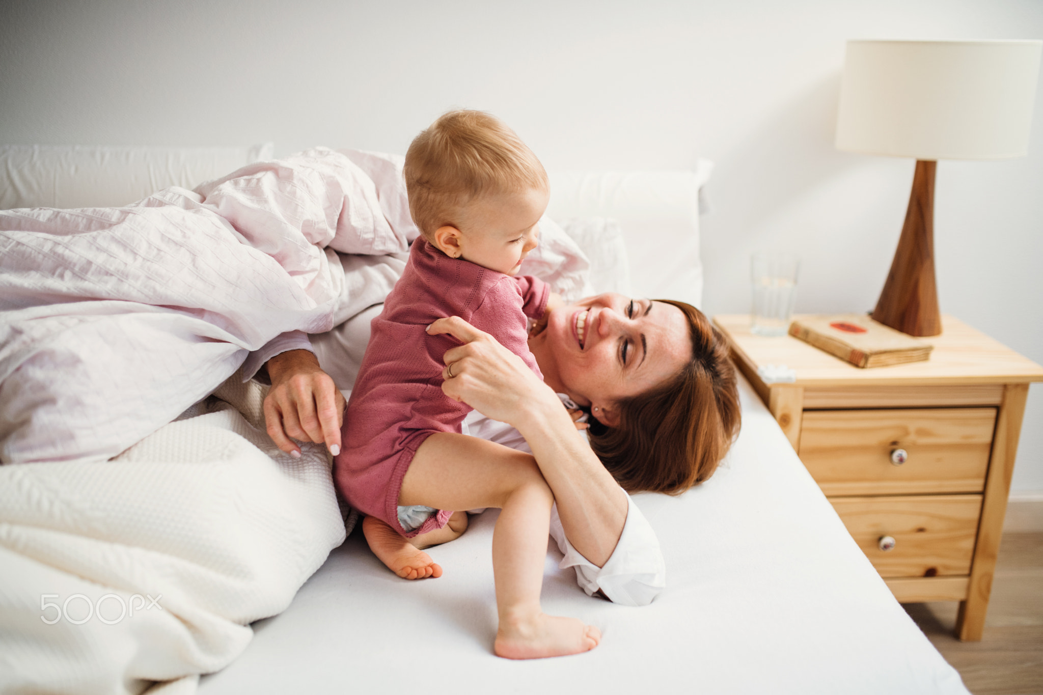 A young mother with little daughter sitting indoors on bed in the morning, playing.