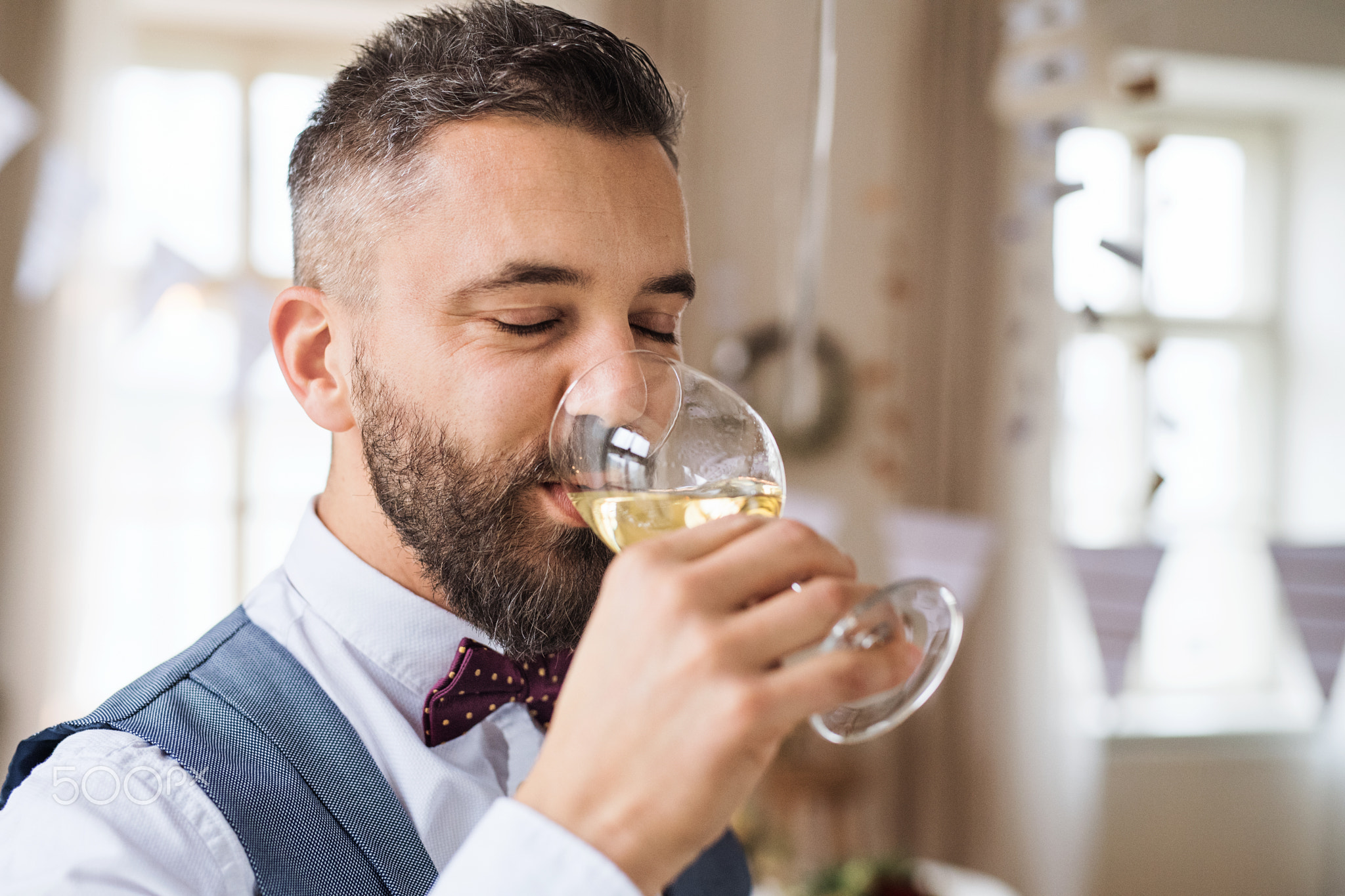A portrait of mature man indoors in a room set for a party, drinking wine.