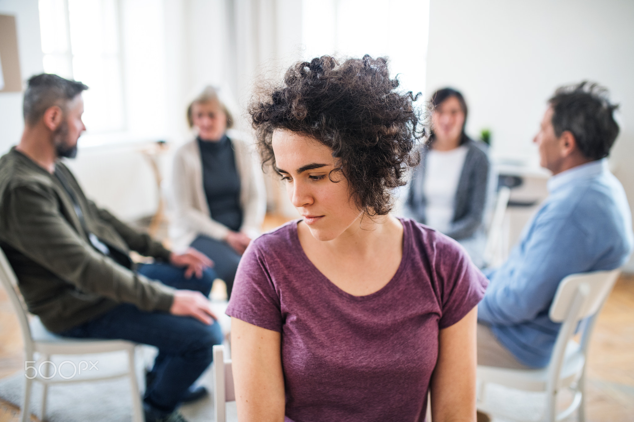 A portrait of young depressed woman during group therapy.