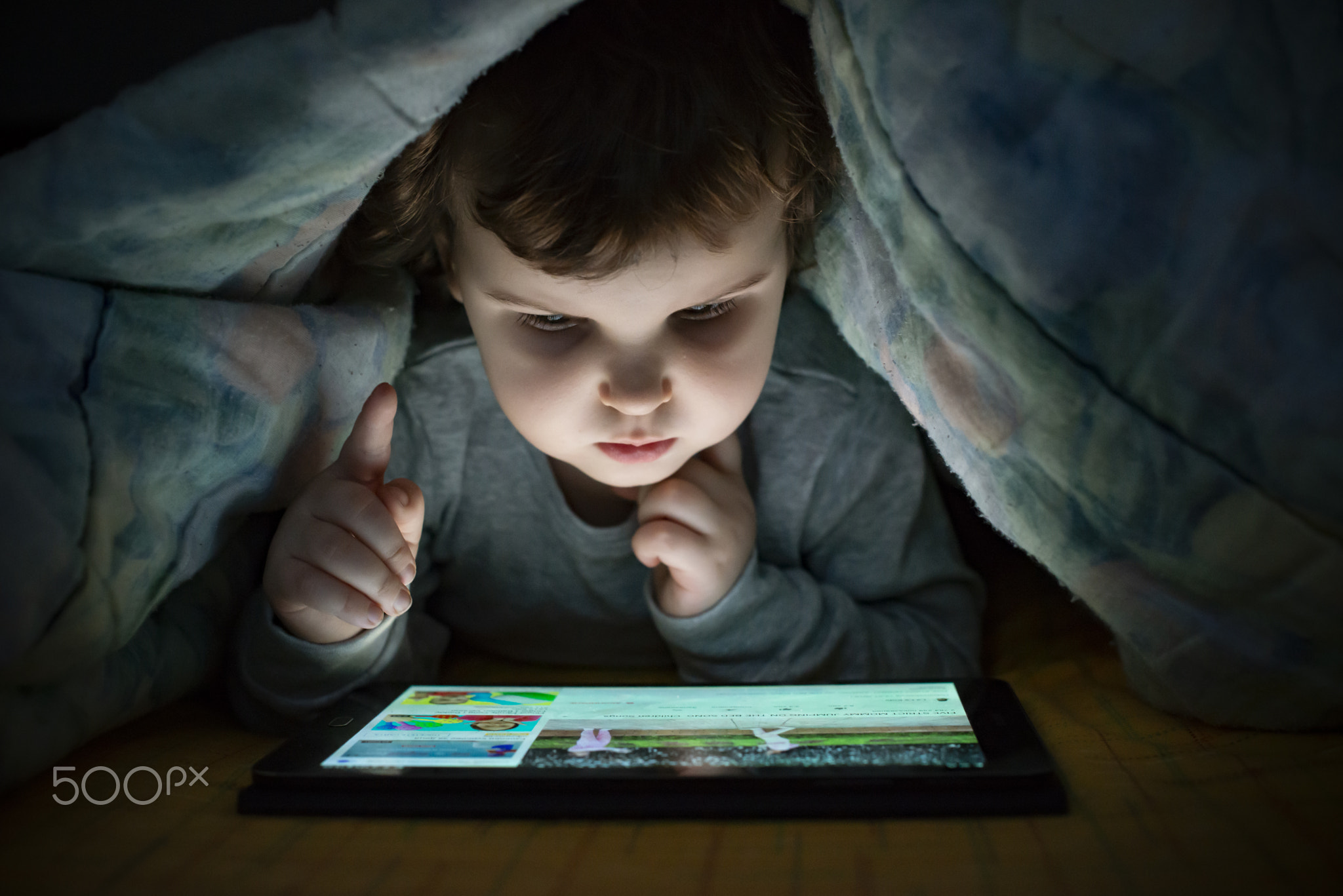 Little girl watching her tablet in the bed. Illuminated child fa