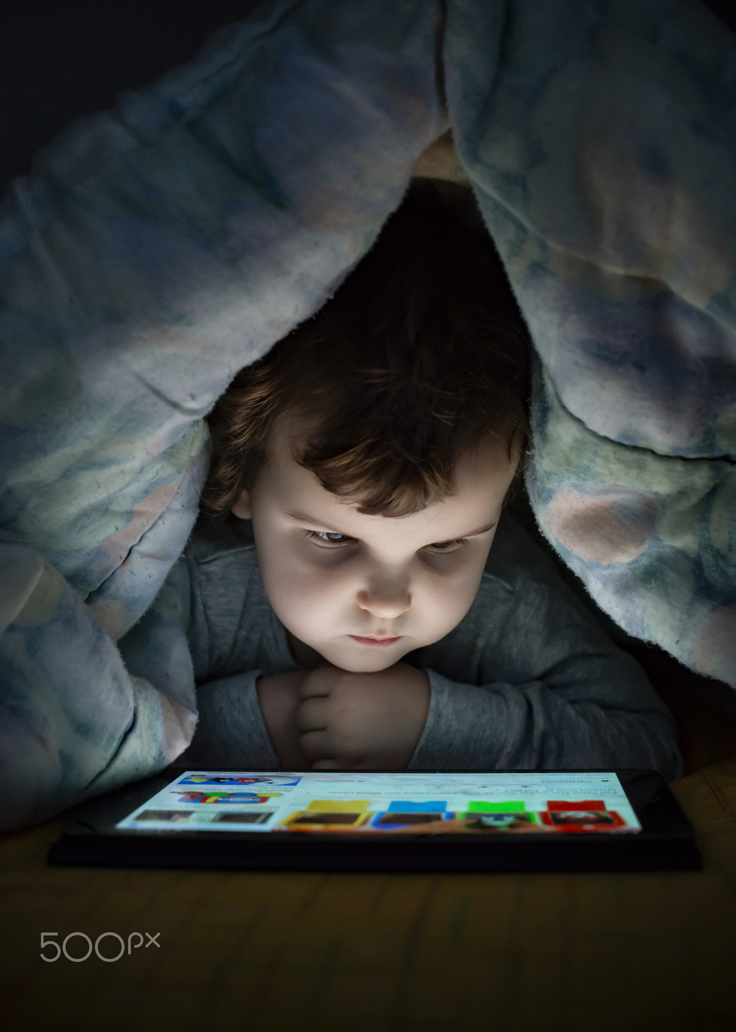 Little girl watching her tablet in the bed. Illuminated child fa