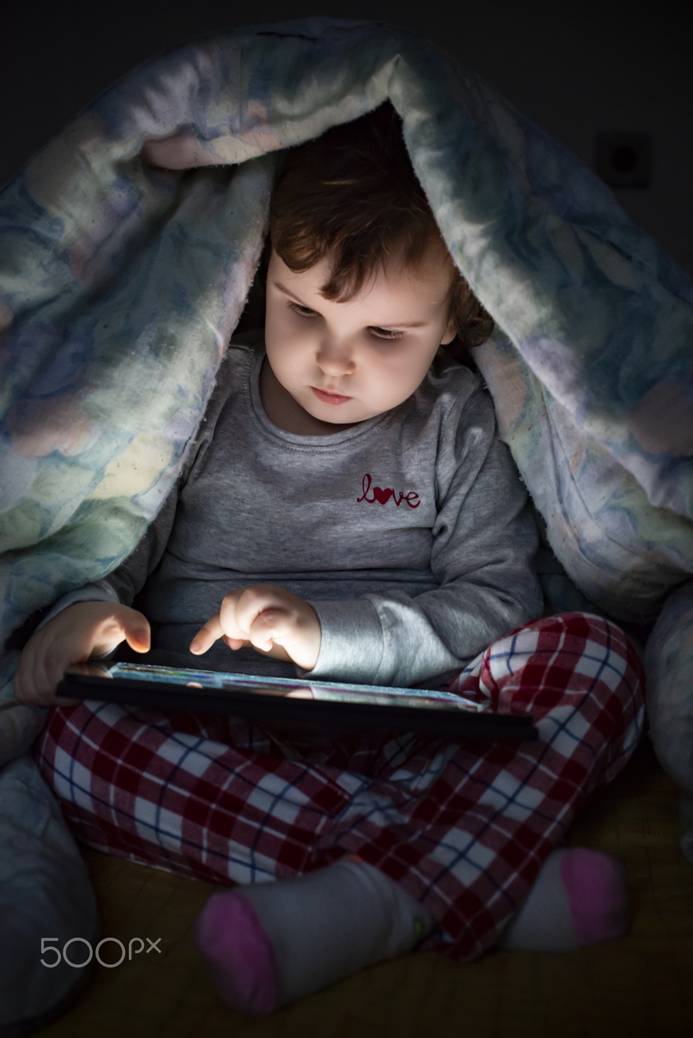 Little girl watching her tablet in the bed. Illuminated child fa