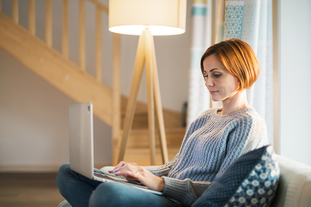 A young woman sitting indoors on a sofa at home, using laptop. by Jozef Polc on 500px.com