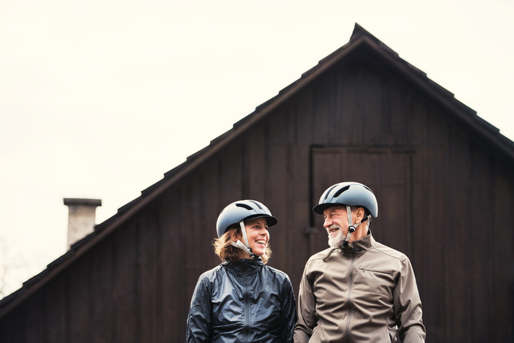 Active senior couple with bike helmets standing outdoors in front of a house. by Jozef Polc on 500px.com