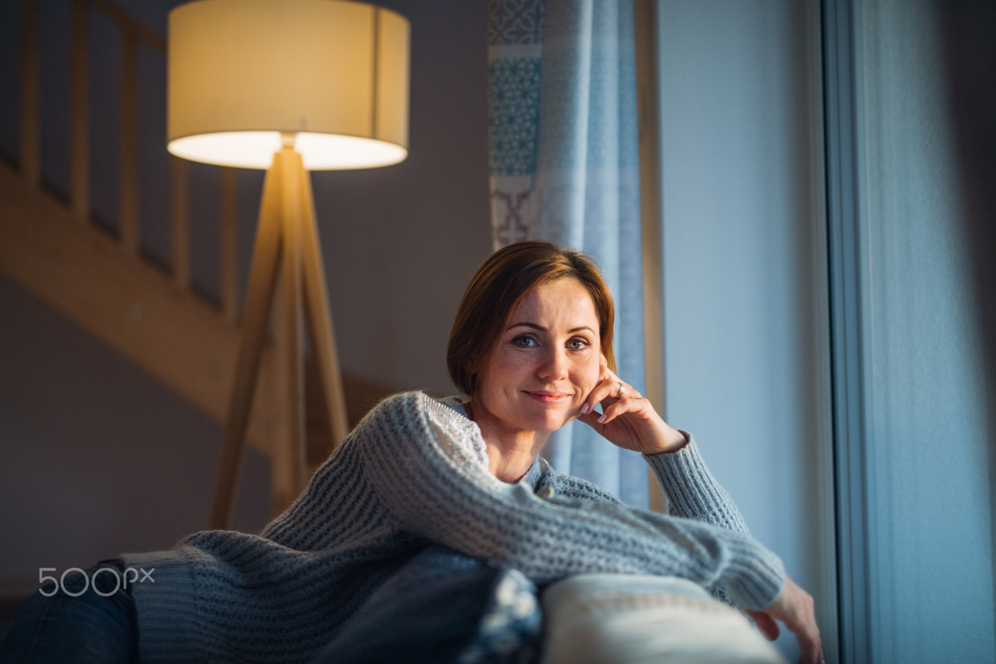 A young woman sitting indoors on a sofa at home, looking at camera.