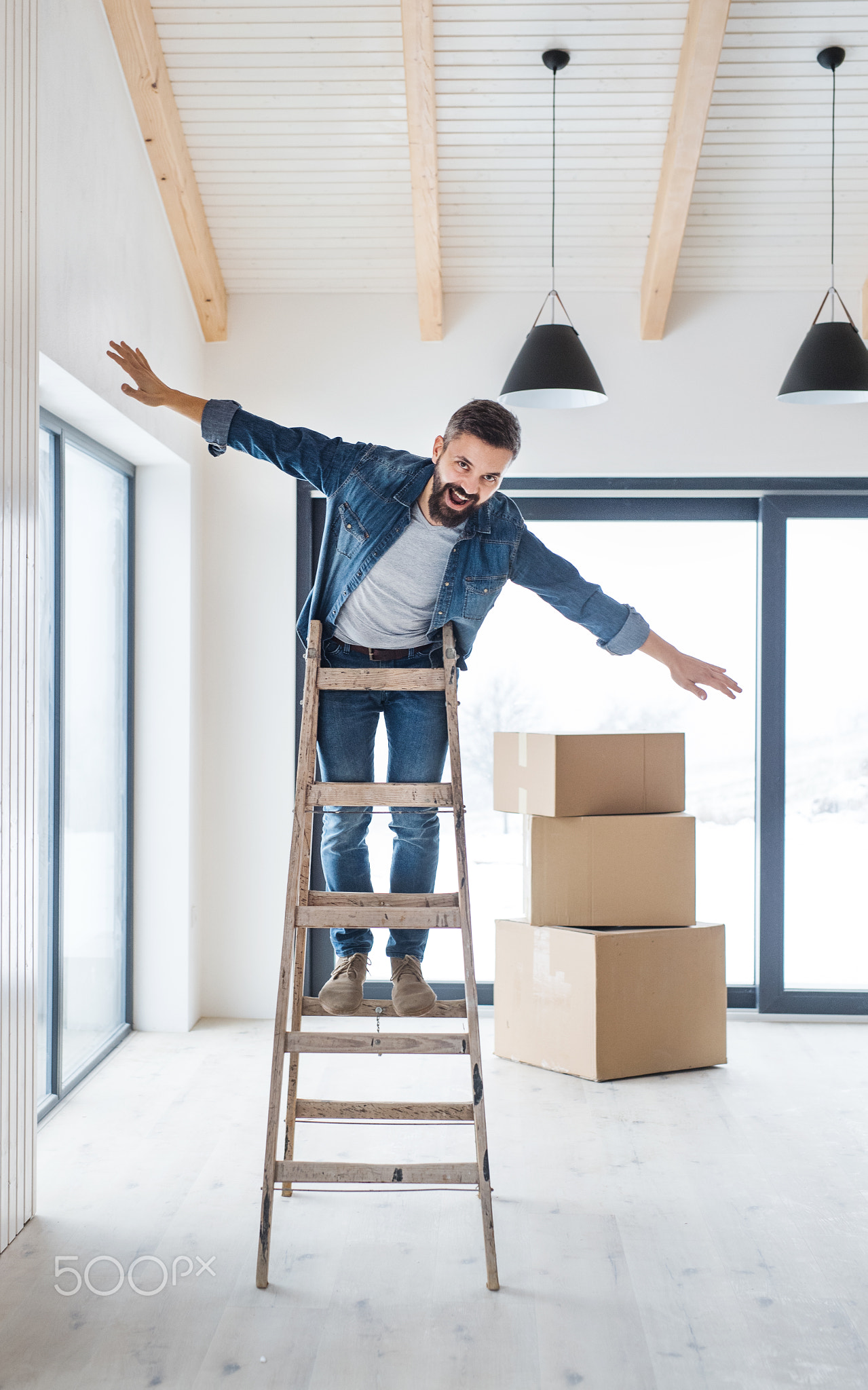 A mature man with cardboard boxes standing on a ladder, furnishing new house.