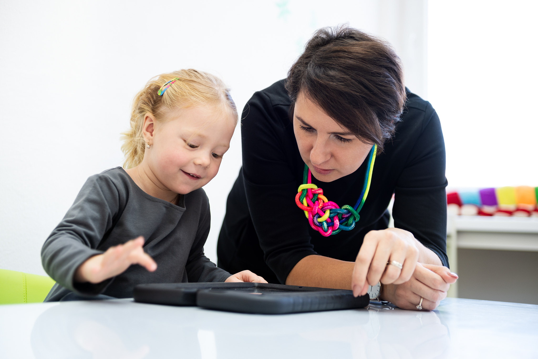 Toddler girl in child occupational therapy session doing playful exercises on a digital tablet...