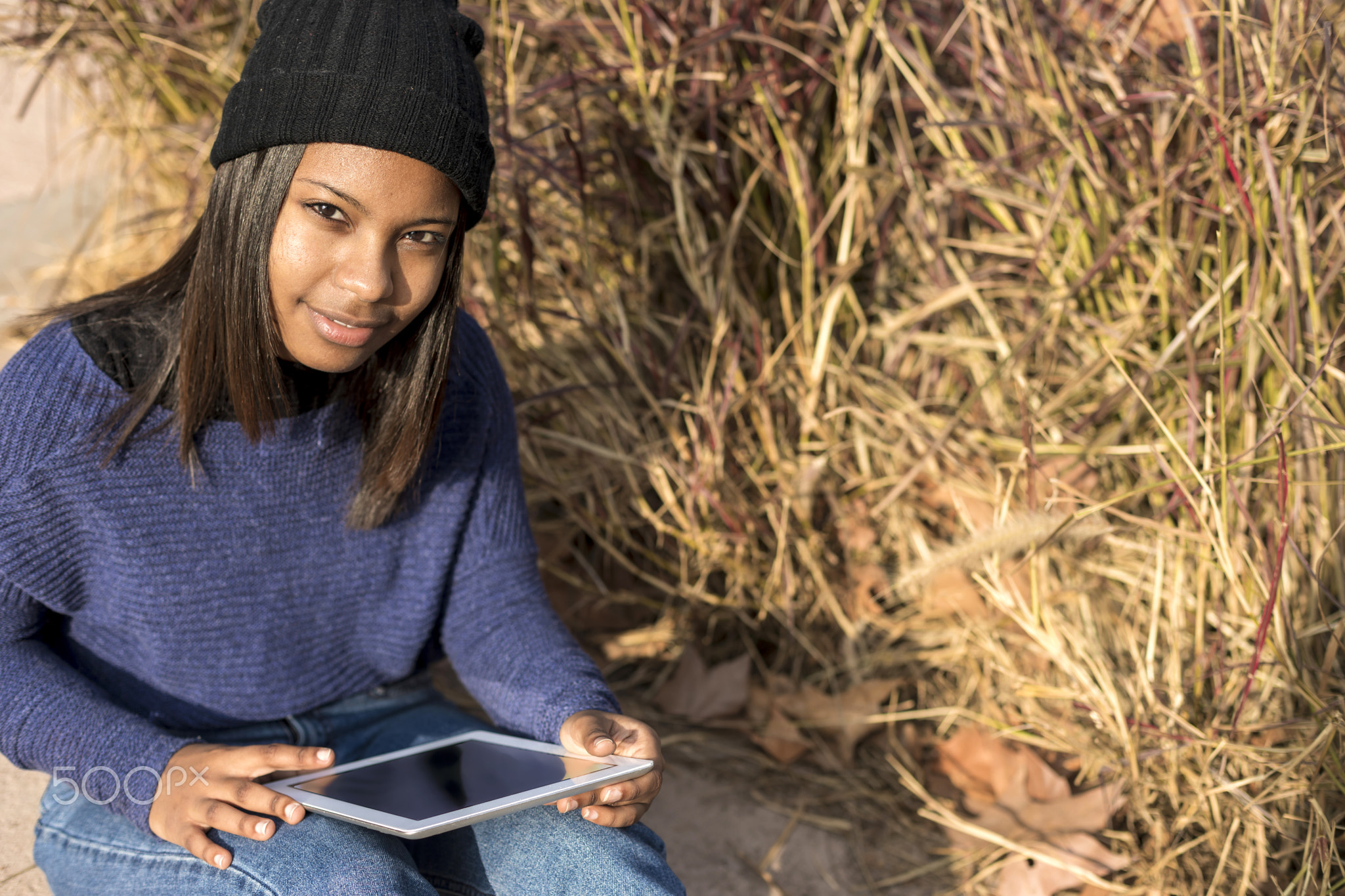 Portrait of a beautiful young smiling african woman using tablet pc computer sitting in the city...