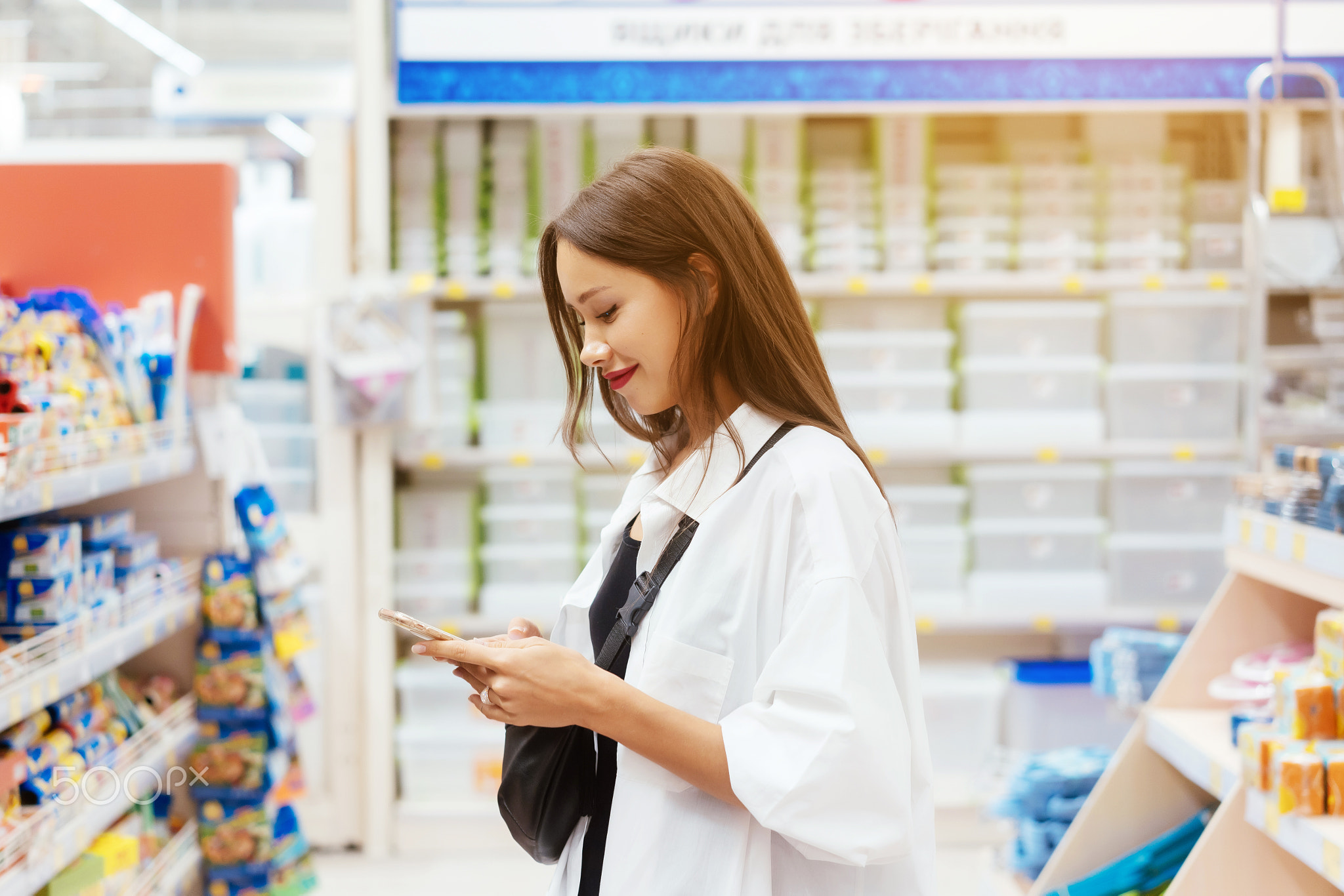 Smiling young woman with smartphone in supermarket