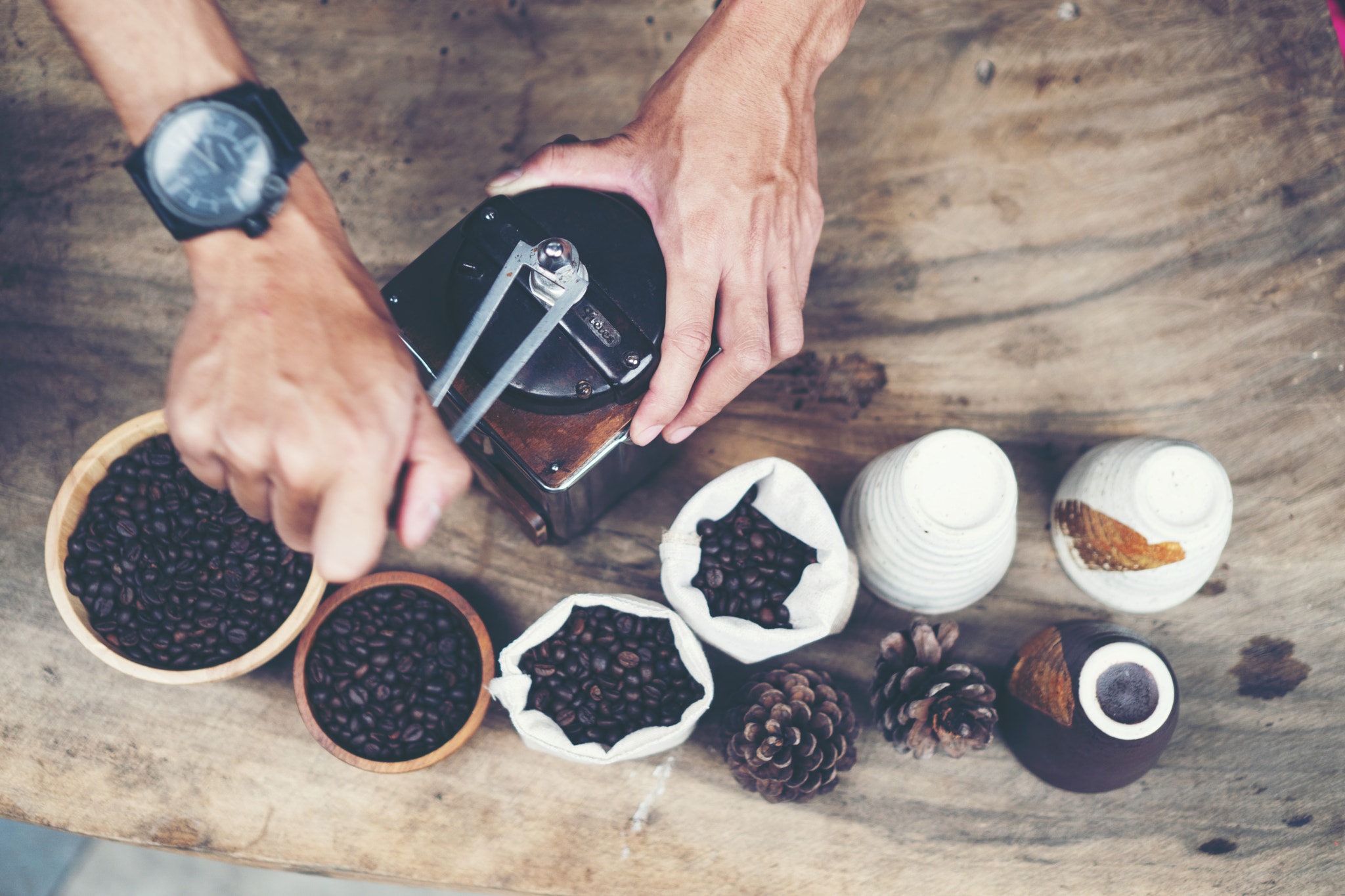 Barista is grinding coffee with a hand coffee grinder.