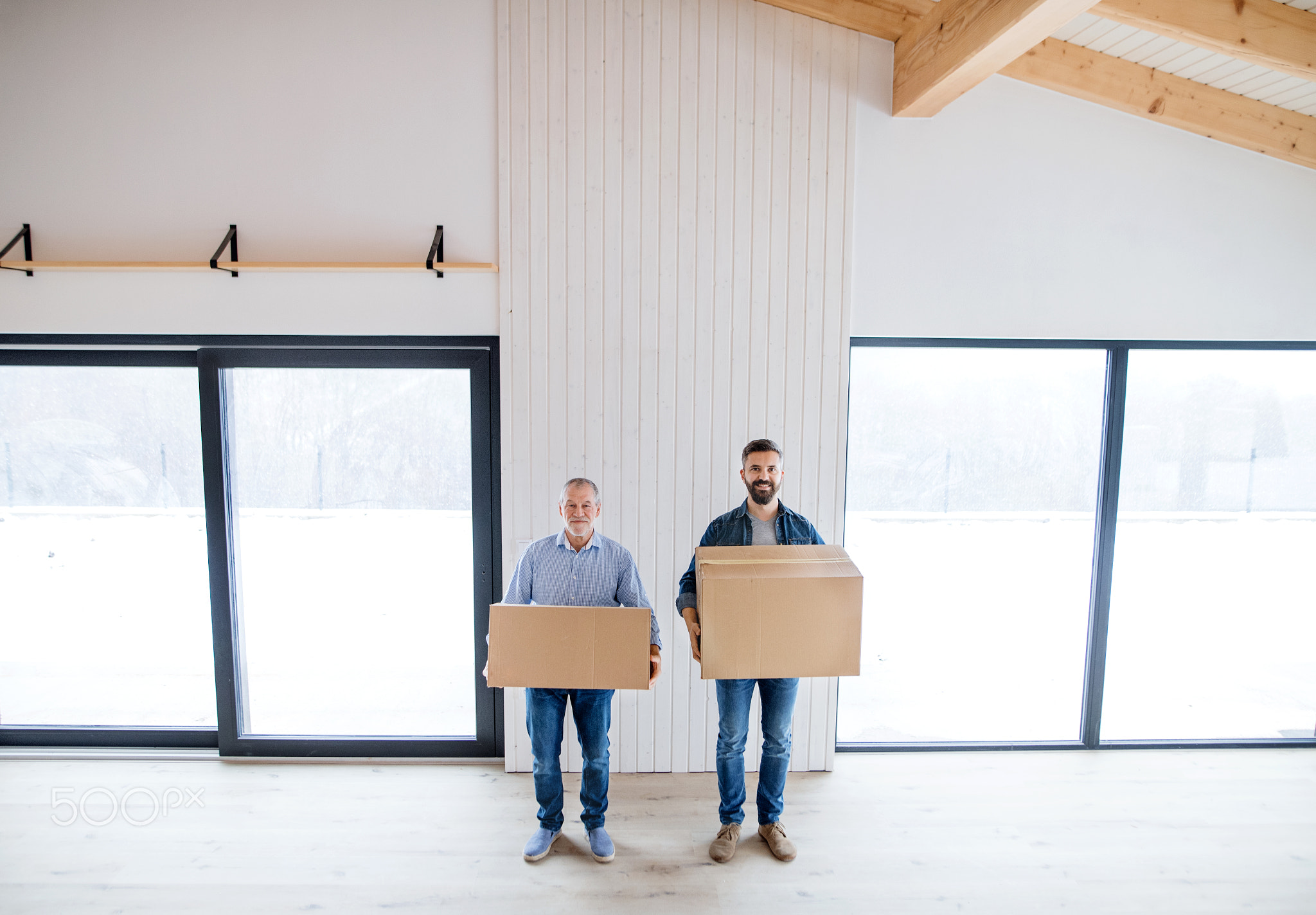 Two men holding cardboard boxes in front of them when furnishing new house.