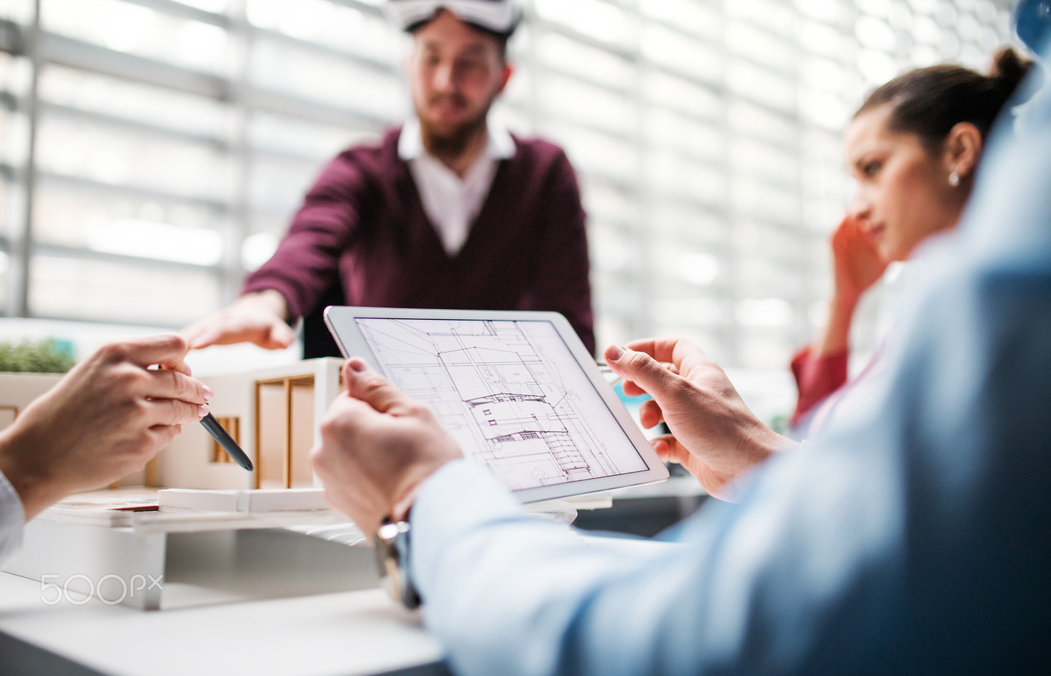 Group of young architects with tablet and model of a house standing in office, talking.