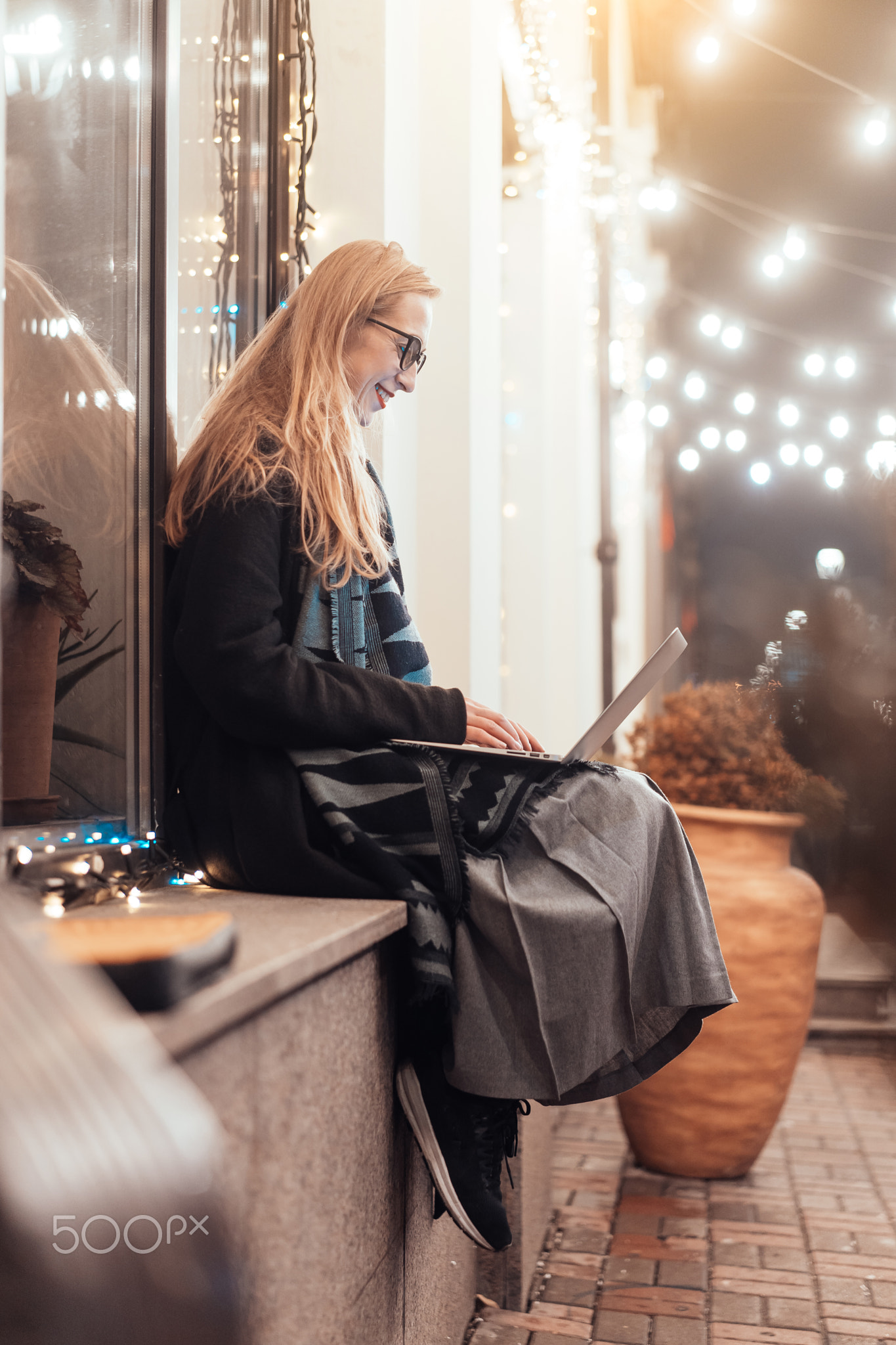 side view of young woman using laptop on street with night city