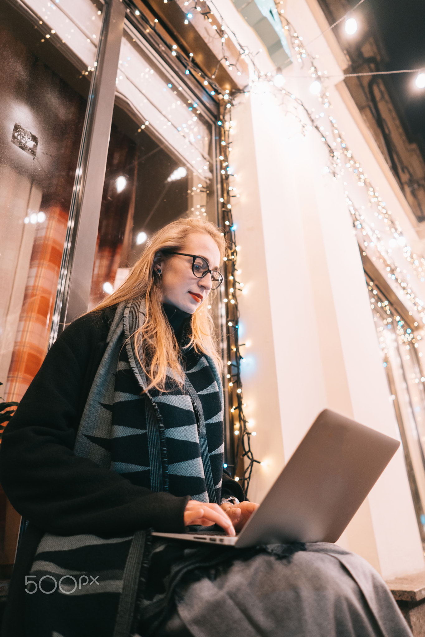 side view of young woman using laptop on street with night city