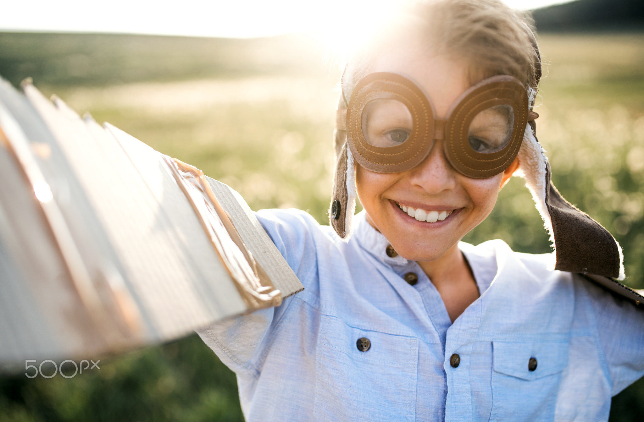 A small boy playing on a meadow in nature, with goggles and wings as if flying.