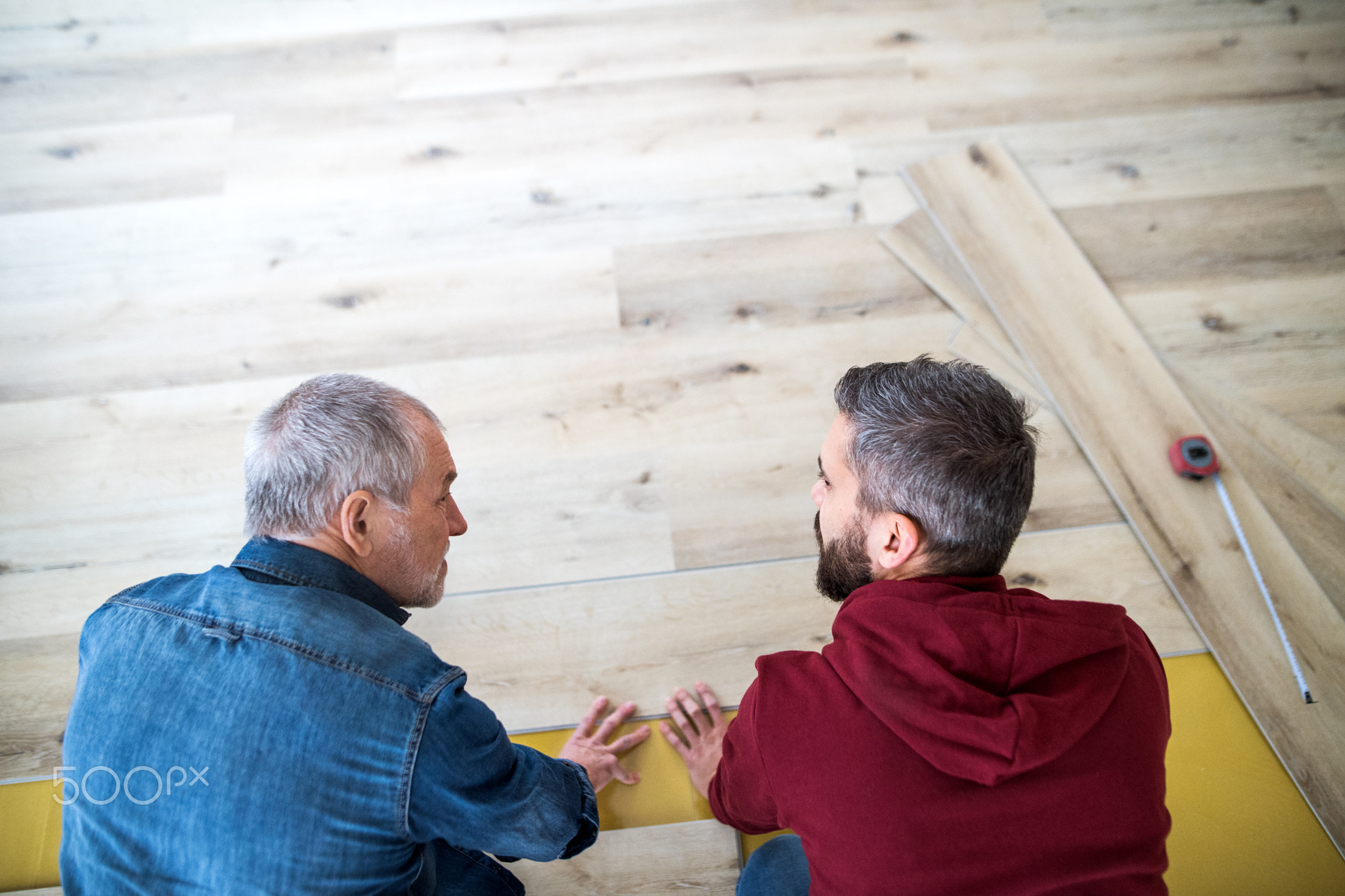 A mature man with his senior father laying wood flooring, a new home concept.