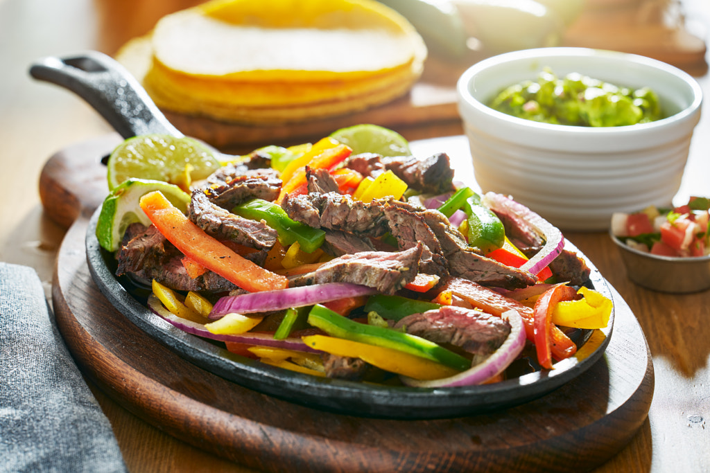 mexican beef fajitas in iron skillet with bell peppers and guacamole on the side by Joshua Resnick on 500px.com