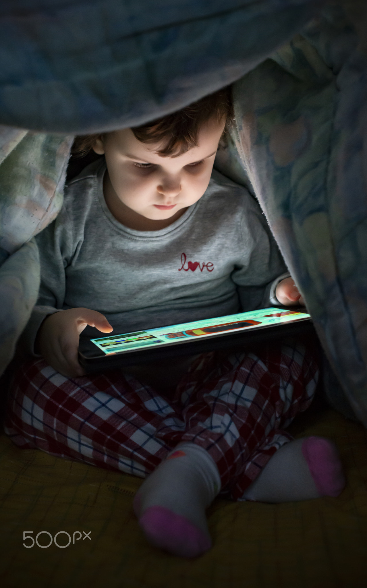 Little girl watching her tablet in the bed. Illuminated child fa