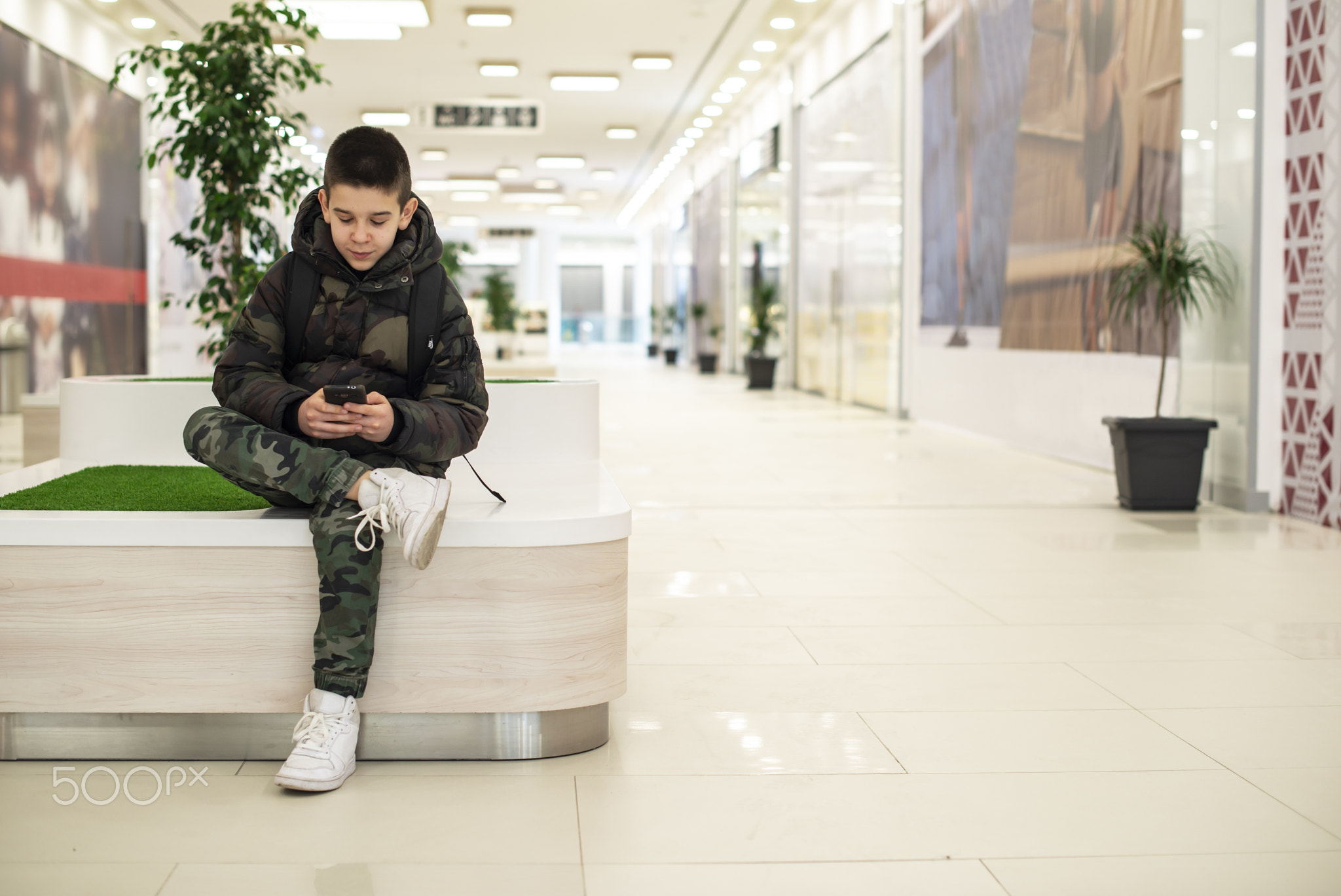 Teenager playing with smartphone in modern commercial center. Te